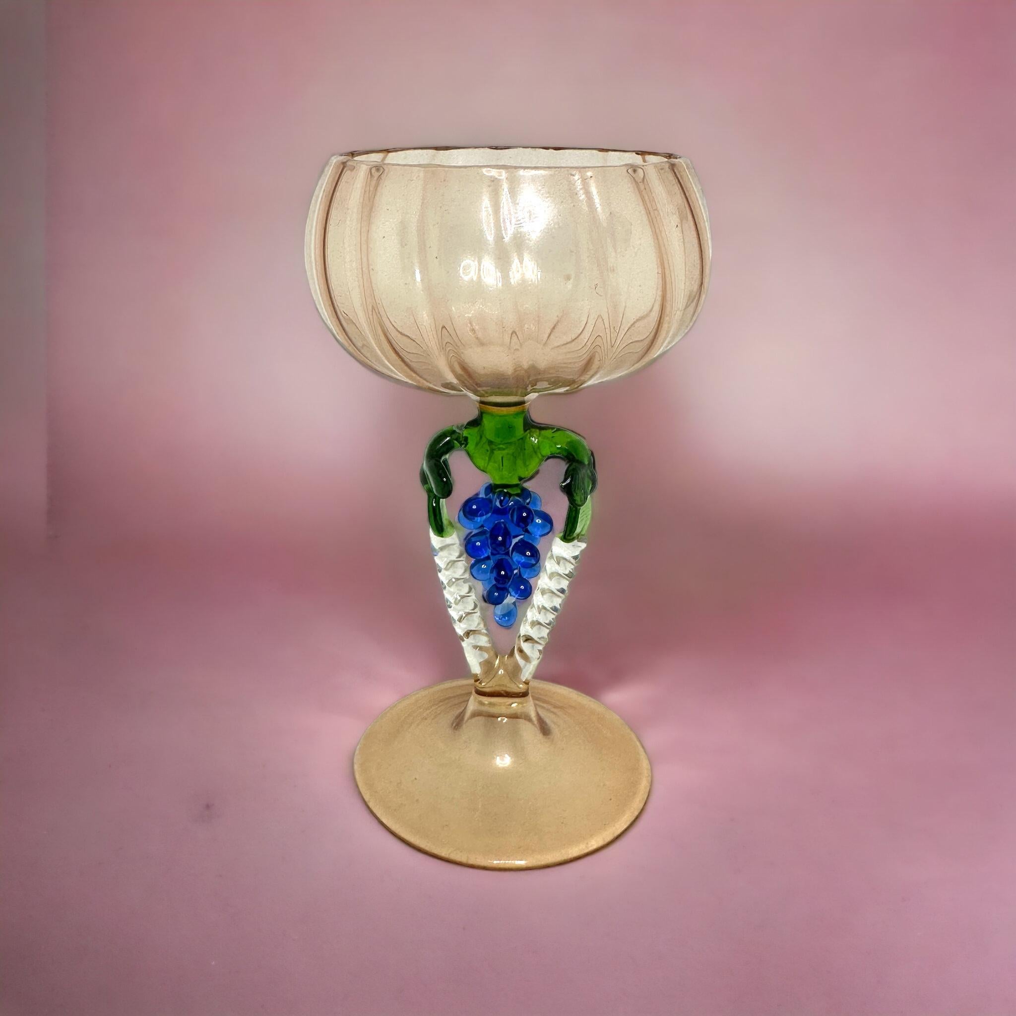 Dies ist ein wunderschönes, einfaches Vintage-Cocktailglas mit Stiel aus Österreich. Es zeigt eine Traubenwelle und ist im Bimini-Stil gehalten. Das hellrosa Glas hat ein geprägtes Design, der Stiel ist eine Weintraube in blauer Farbe. Der Sockel