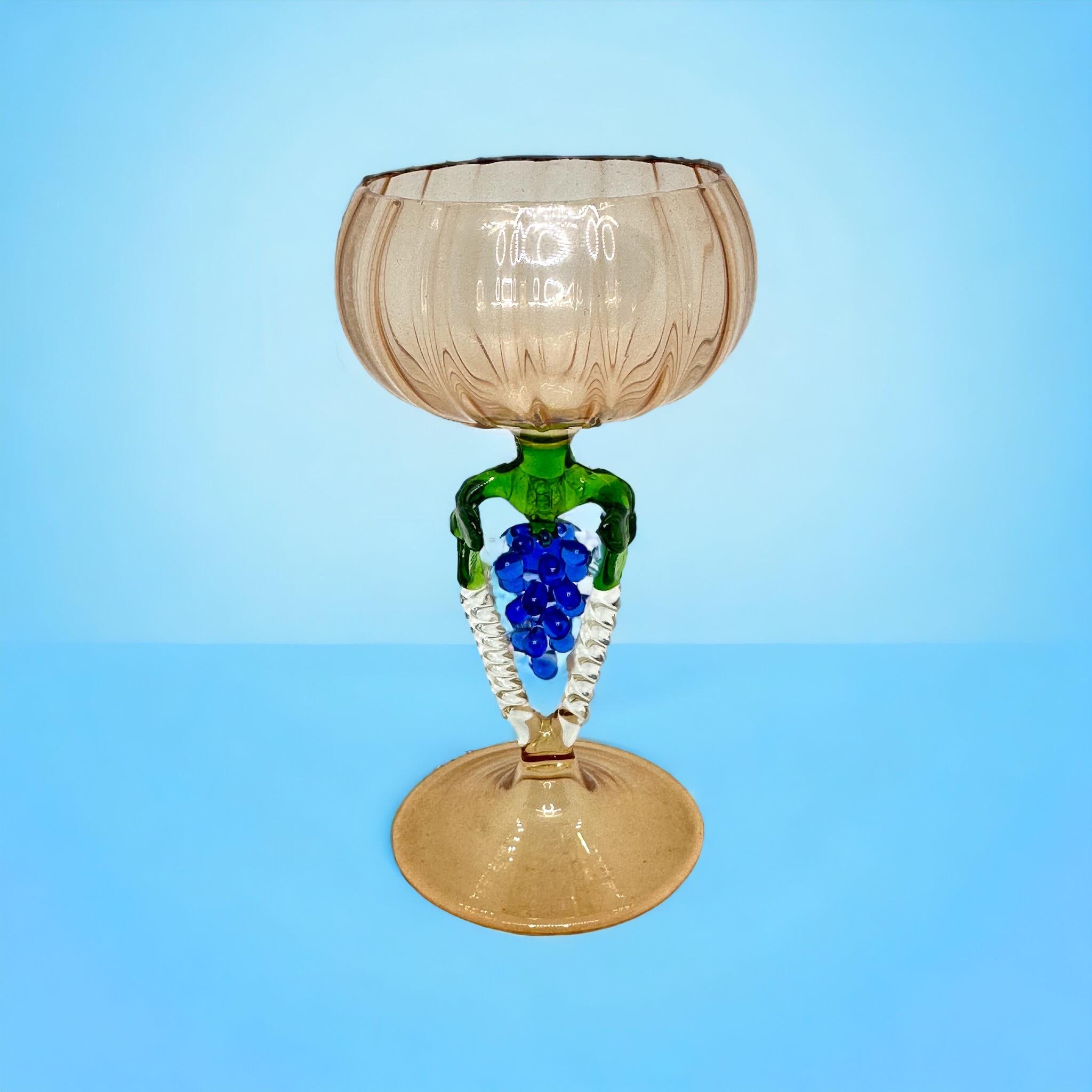 Dies ist ein wunderschönes, einfaches Vintage-Cocktailglas mit Stiel aus Österreich. Es zeigt eine Traubenwelle und ist im Bimini-Stil gehalten. Das hellrosa Glas hat ein geprägtes Design, der Stiel ist eine Weintraube in blauer Farbe. Der Sockel
