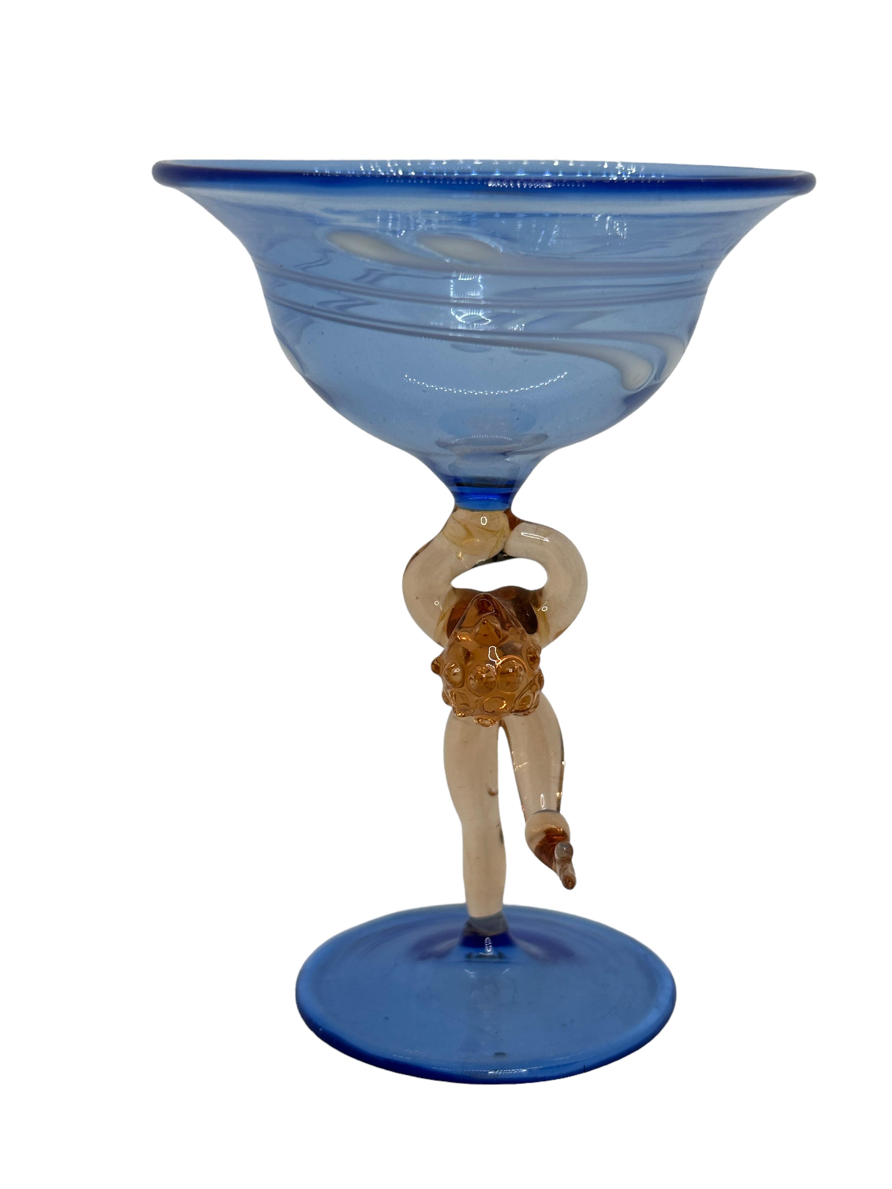 Se trata de una preciosa copa de cóctel con tallo de una sola añada, procedente de Austria. Presenta un eje de mujer desnudo y es de estilo artístico Bimini. El cristal azul tiene un diseño en relieve, el tallo es una dama desnuda de color rosáceo.