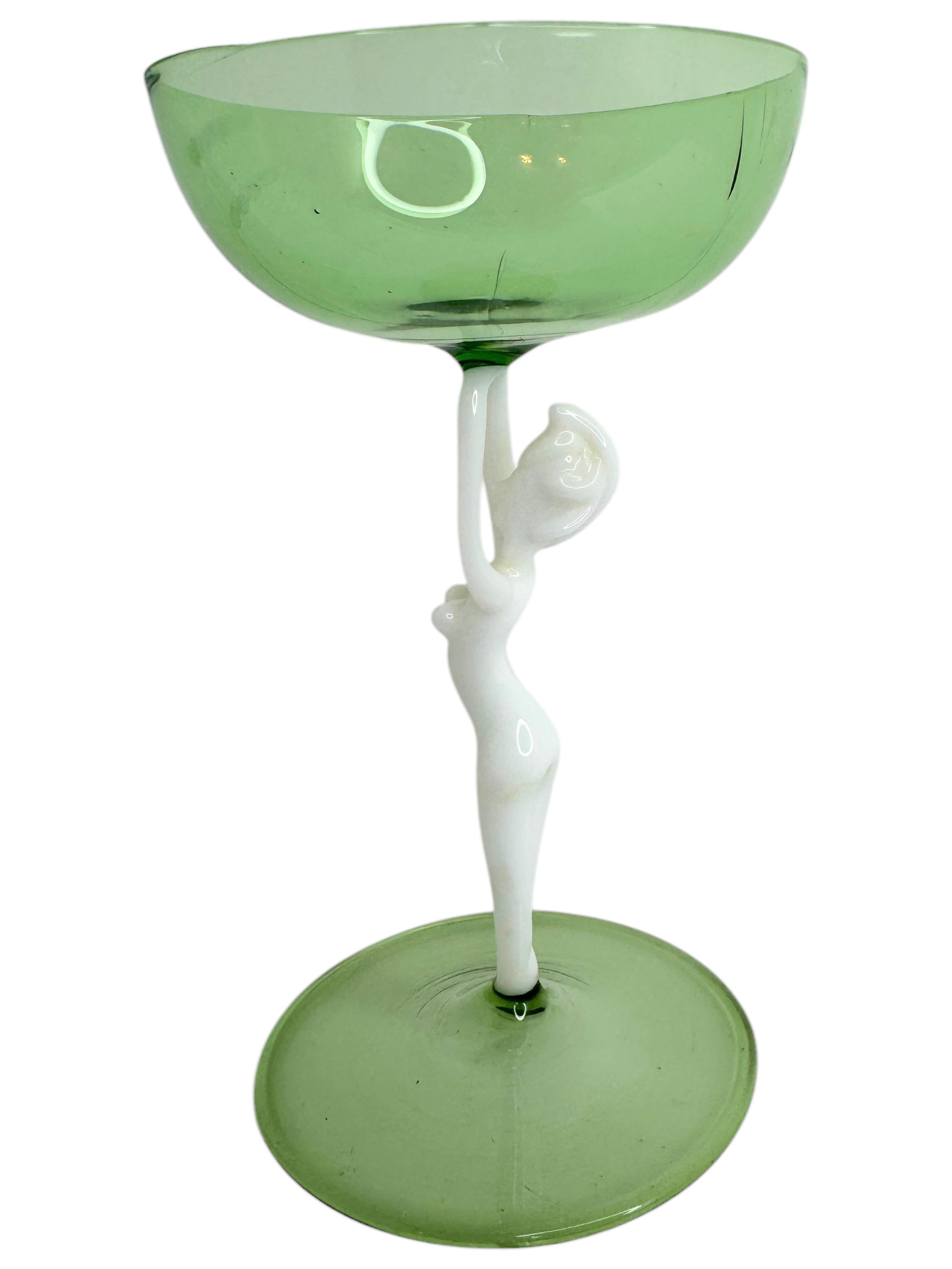 Il s'agit d'un magnifique verre à cocktail à pied d'Autriche. Il présente une tige de femme nue et est dans le style artistique Bimini. Le verre vert a un design en relief, la tige est une femme nue de couleur blanche. La base est un beau verre