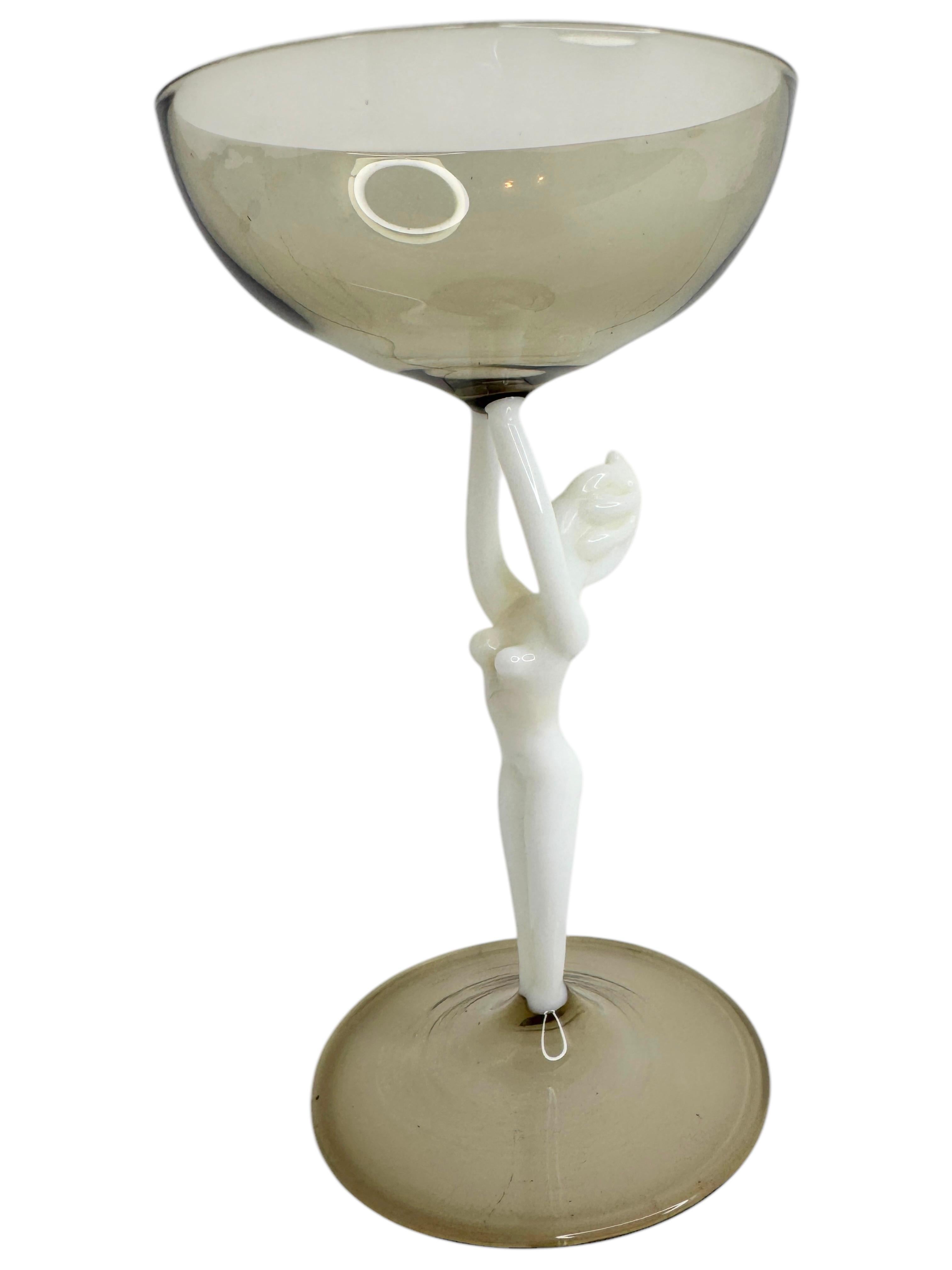 Se trata de una preciosa copa de cóctel con tallo de una sola añada, procedente de Austria. Presenta un eje de mujer desnudo y es de estilo artístico Bimini. El cristal gris tiene un diseño en relieve, el tallo es una dama desnuda de color blanco.