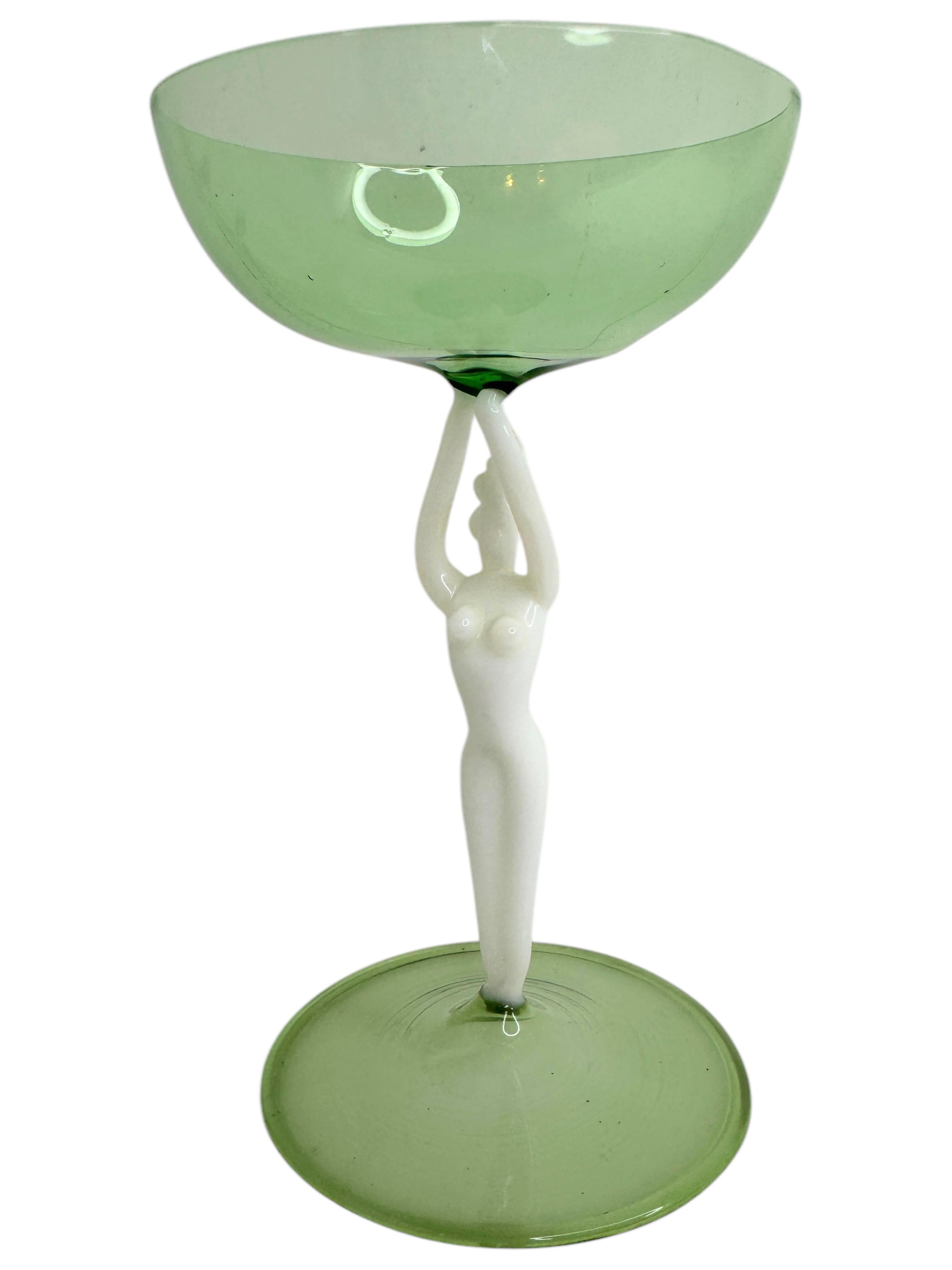 Se trata de una preciosa copa de cóctel con tallo de una sola añada, procedente de Austria. Presenta un eje de mujer desnudo y es de estilo artístico Bimini. El cristal verde tiene un diseño en relieve, el tallo es una dama desnuda de color blanco.