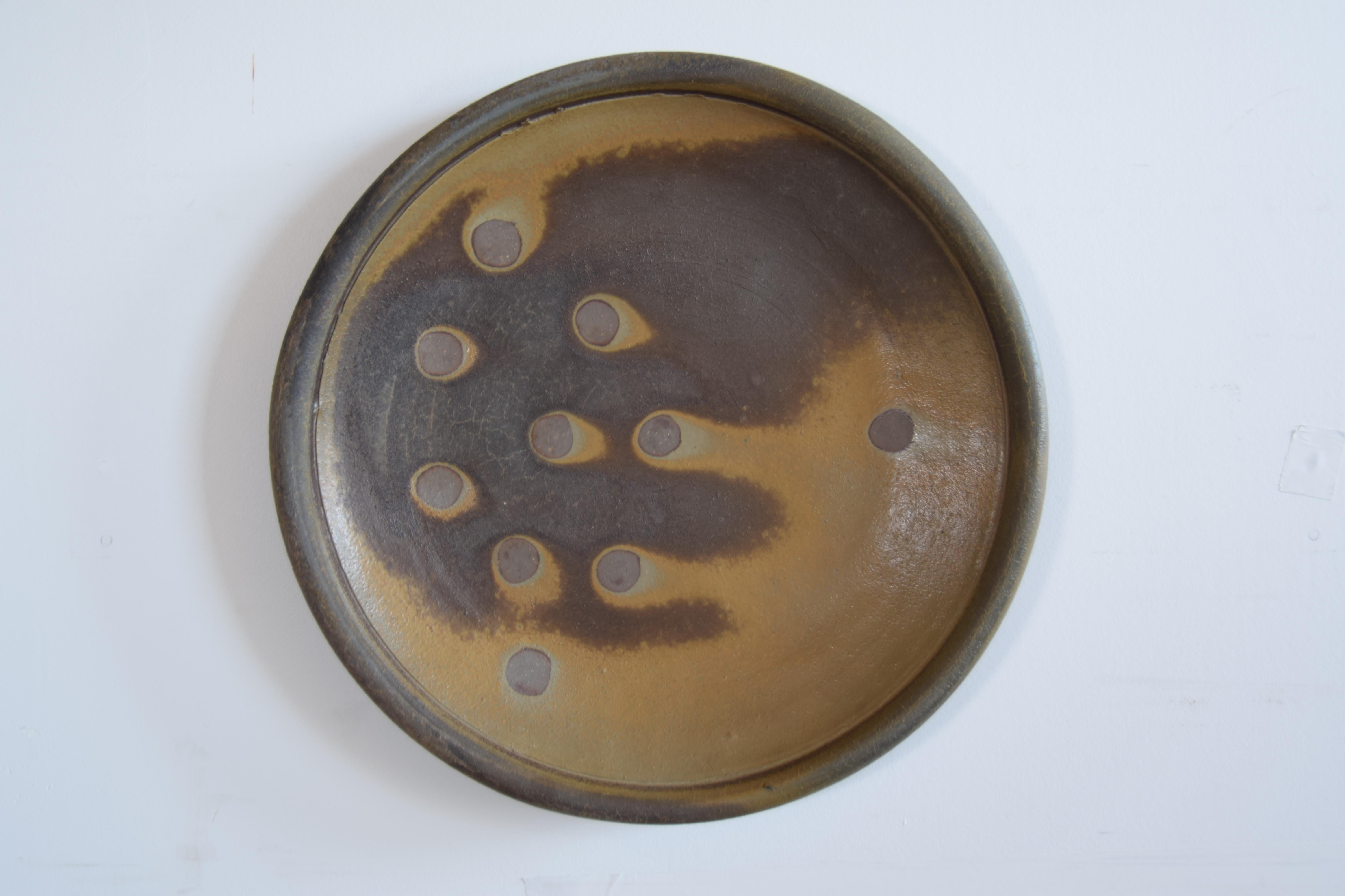 Studio pottery charger, circa 1979. The charger has the ability to be hung on a wall, due to the fact that the artist provided for two small holes on the foot where wire could be strung. However, it can also be placed flat on a horizontal surface,