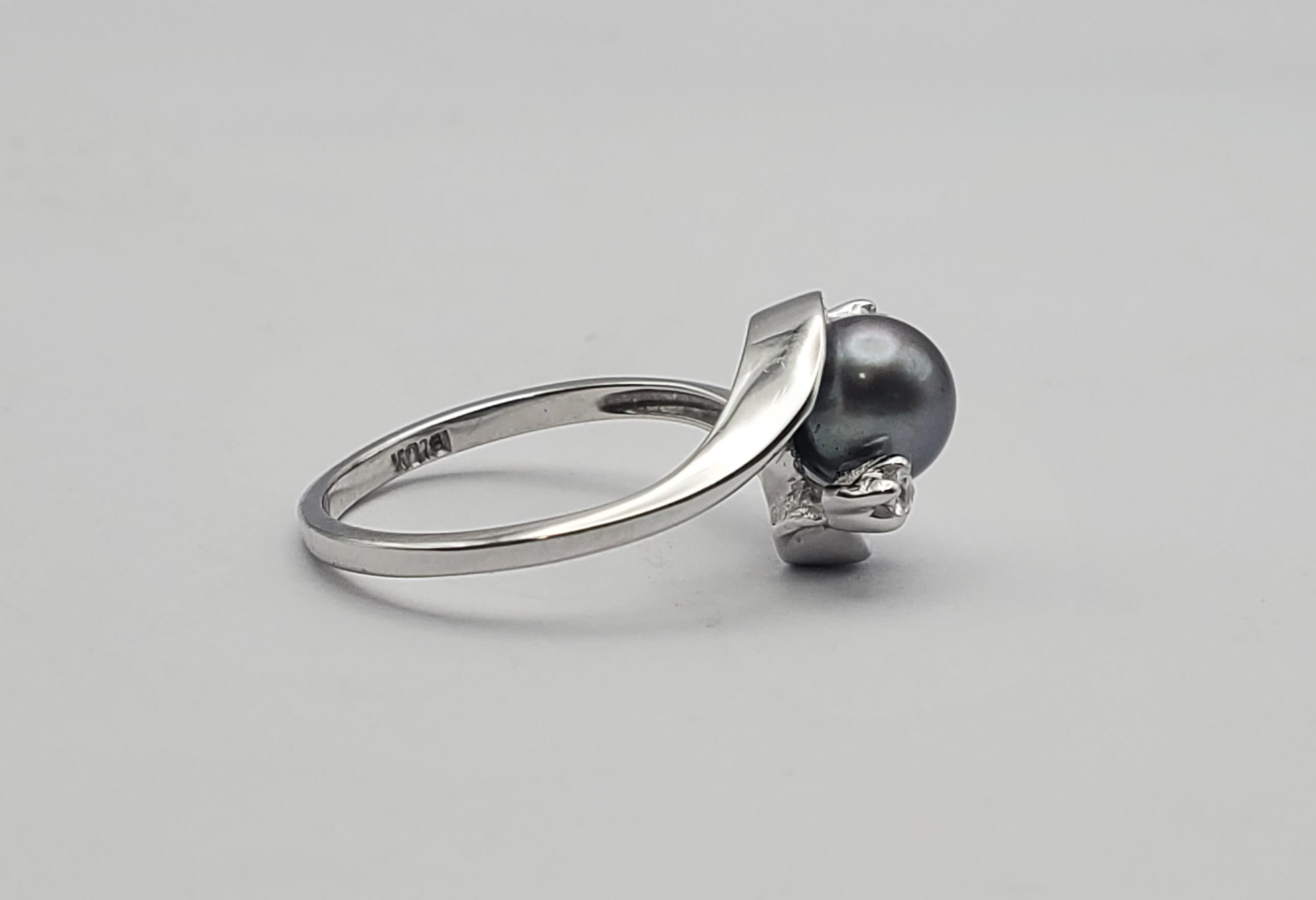 Stunning Tahitian pearl and diamond ring. The pearl has an smoky grey color with undertones of purple and green. The design of the ring is a bypass style with the sides of the pearl protected by two curves of gold, each tipped with a single round
