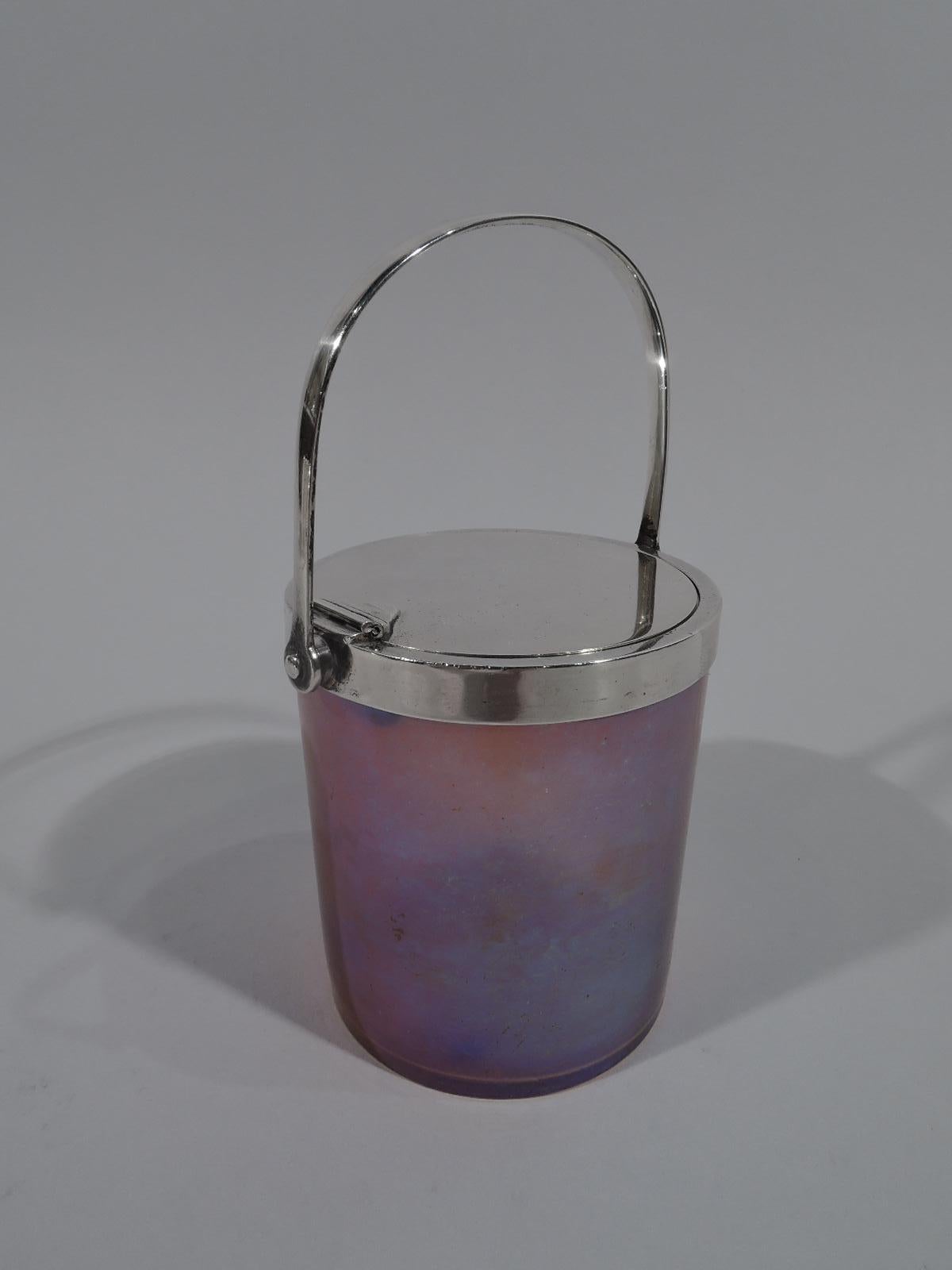 Beautiful Art Nouveau sterling silver and Favrile glass jam pot, circa 1910. Made by Tiffany & Co. in New York. Cylindrical with straight sides. Glass nuanced purple and gold. Pontil mark. Silver collar with flat hinged cover that opens by lowering