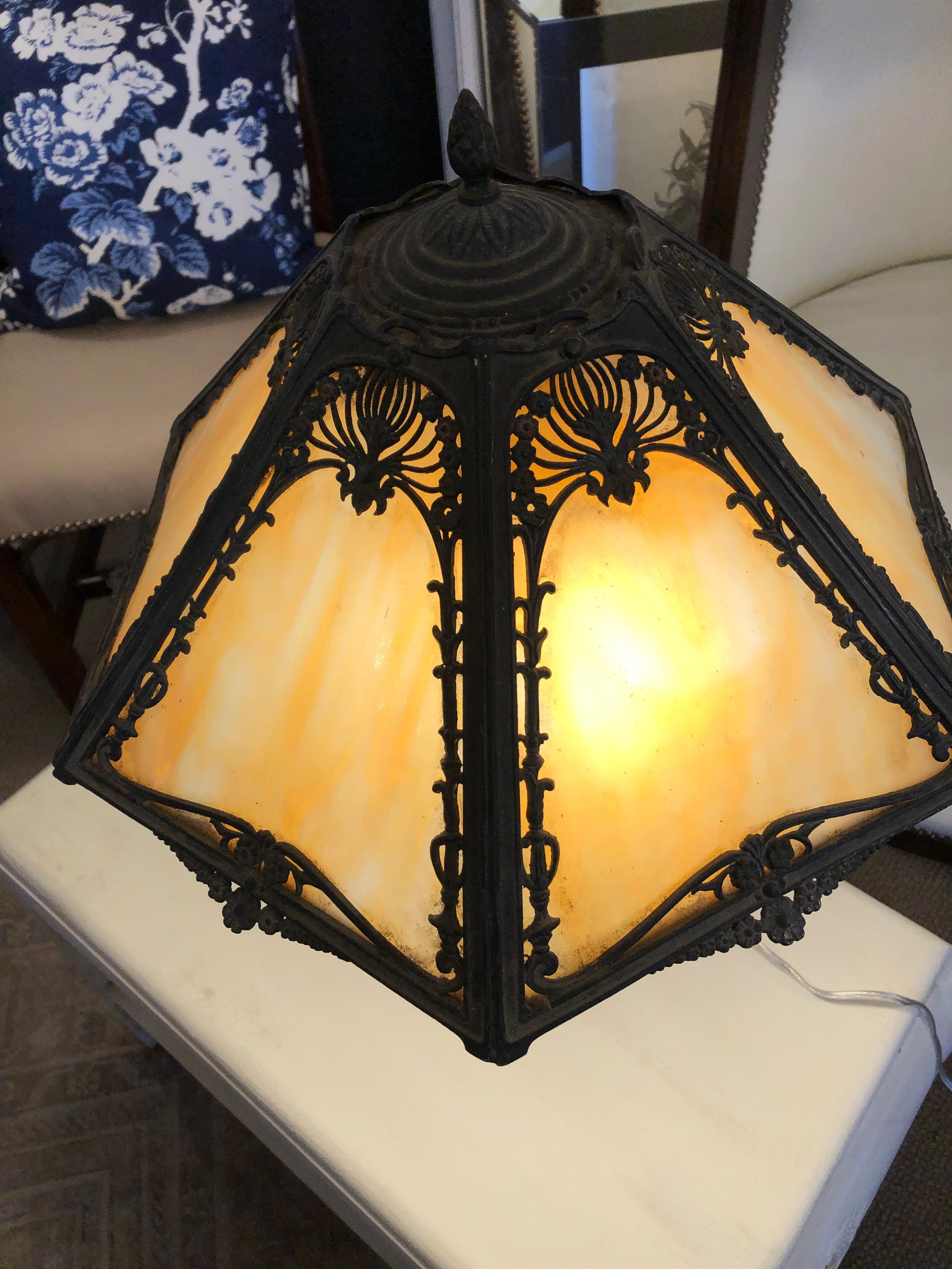 Antique cast iron Tiffany style table lamp having meticulous details and warm butterscotch art glass that glows when illuminated.