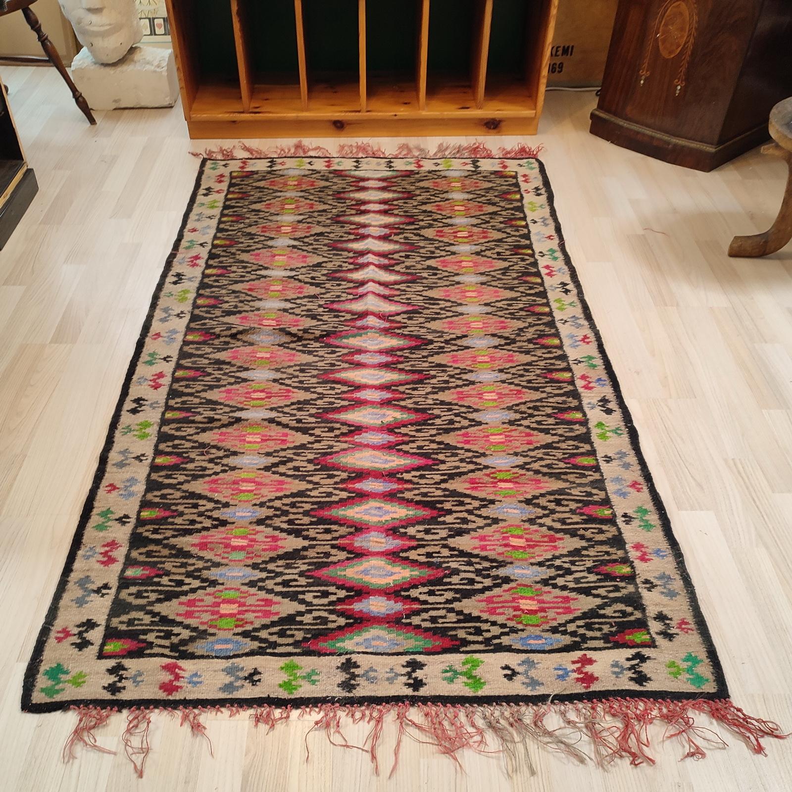 Turkish Kilim, of the 1940s.
This colorful antique kilim has a bold presence provided by its graphic geometric motifs realized in shades of vivid green, sky blue, dark red, olive, and accents of yellow, all against a black background with a beige