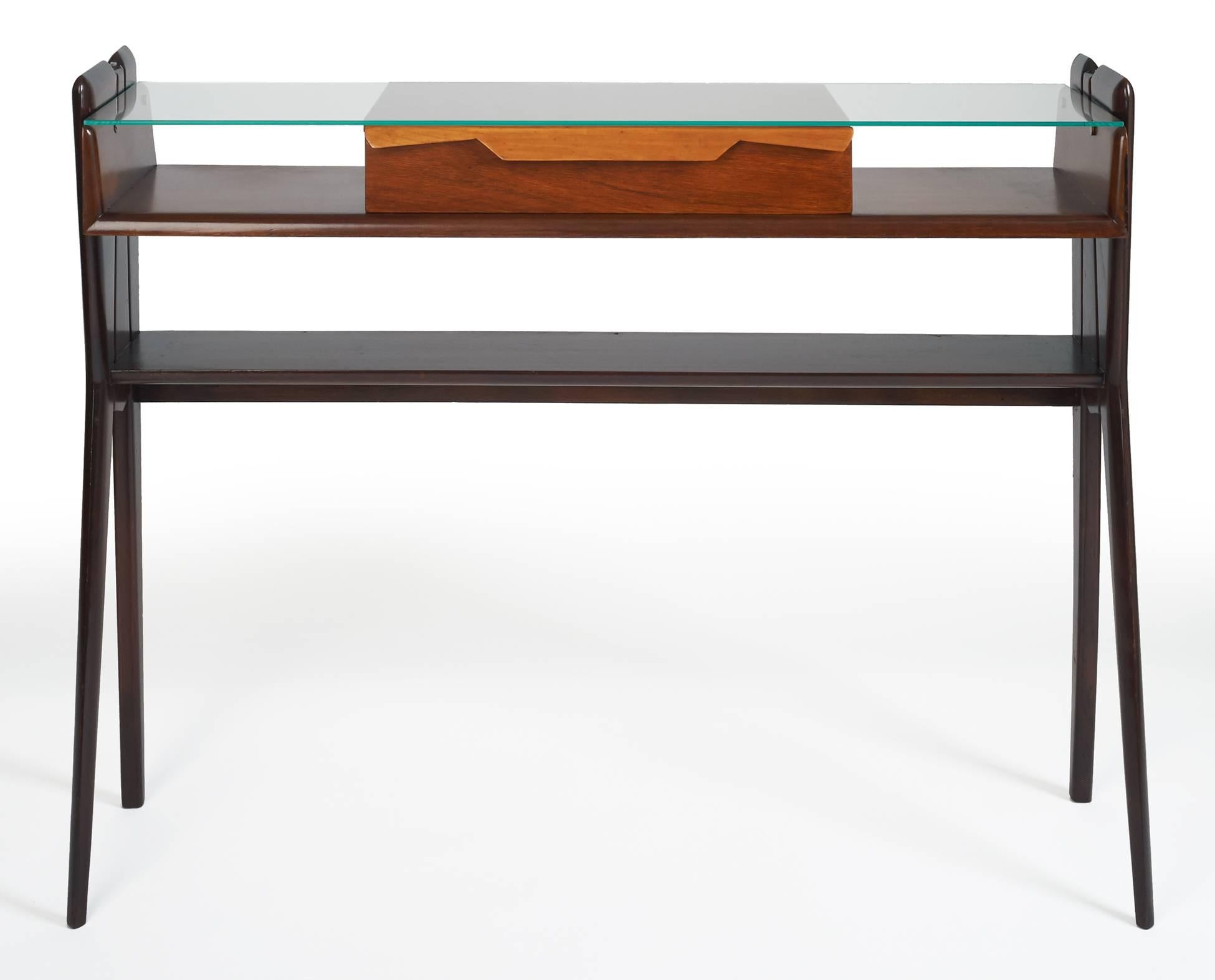 Ico Parisi (1916–1996), attributed to
A lissome, organic three-shelf console table in rosewood, with playful, geometric dual-tone central drawer and a glass top raised on slender, finely sculpted and angled legs.


 