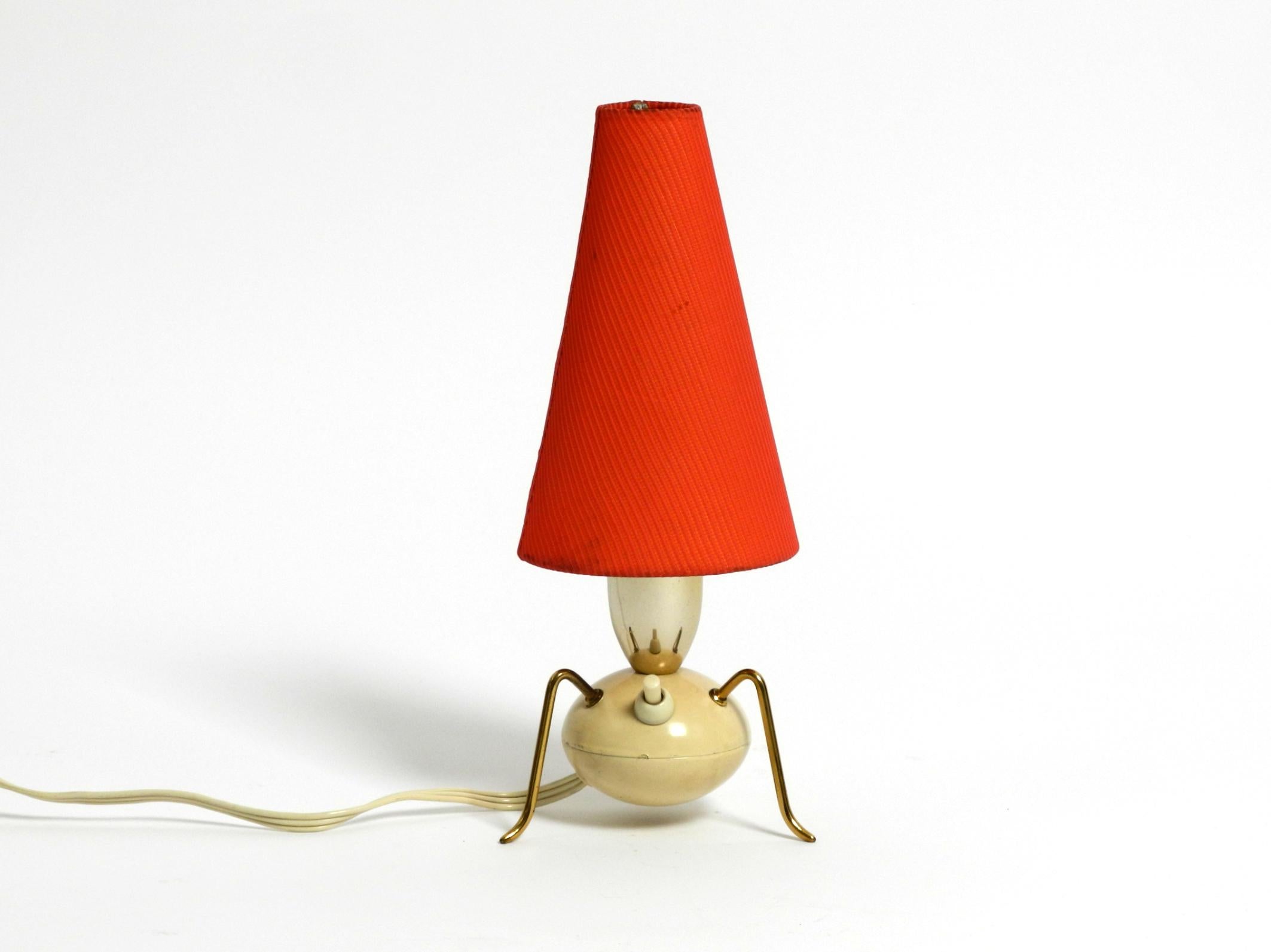 Magnifique lampe de table tripode en laiton avec abat-jour en tissu rouge d'origine.
Design/One typique des années 1950 en laiton et métal peint en beige.
La base avec les pieds en laiton rappelle une araignée.
Très bon état vintage et entièrement