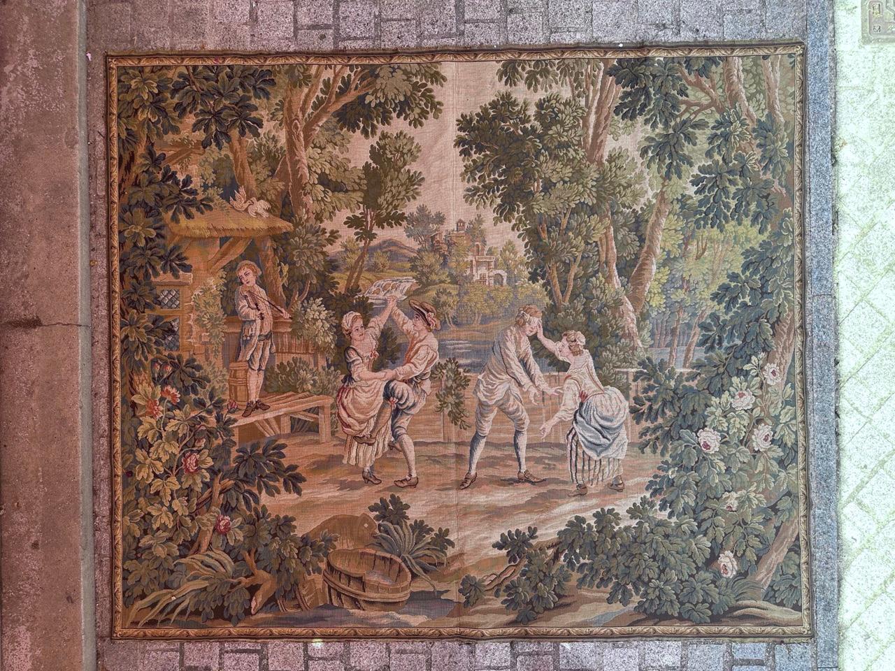 Discover the exquisite charm of our midcentury French tapestry, featuring a captivating design reminiscent of an 18th-century masterpiece. Depicting the romantic dance and play of lovers, this tapestry boasts vibrant colors and is intricately woven