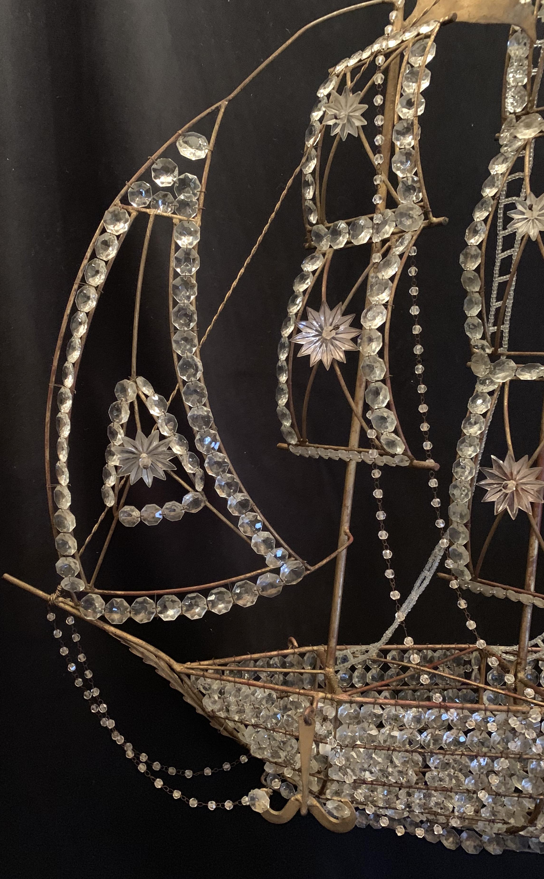 Maravillosa araña de barco, bellamente detallada con un casco de cristal y detalles de estrellas de cristal. Equipada con 5 luces interiores y un farol, así como con escaleras de cuentas y velas que conducen a las banderas de tole ondeando desde