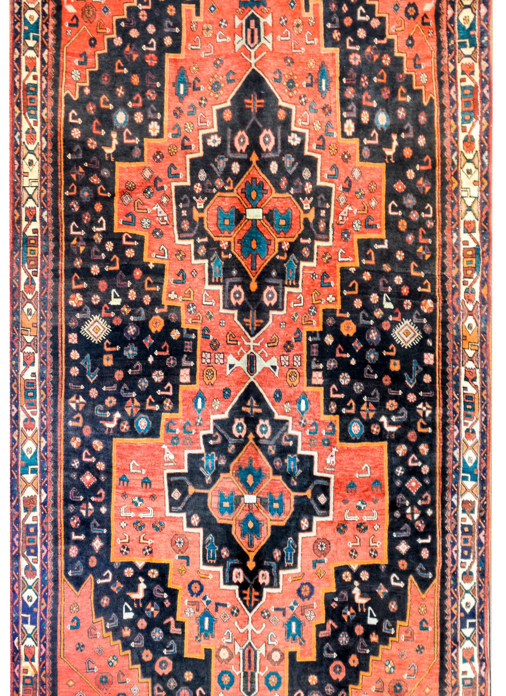 A beautiful vintage Persian Mazleghan rug with two large red stepped diamonds with stylized flowers and chickens on a black field of similar stylized flowers and chickens. The border is complex with bold stylized flowers and thin geometric patterned