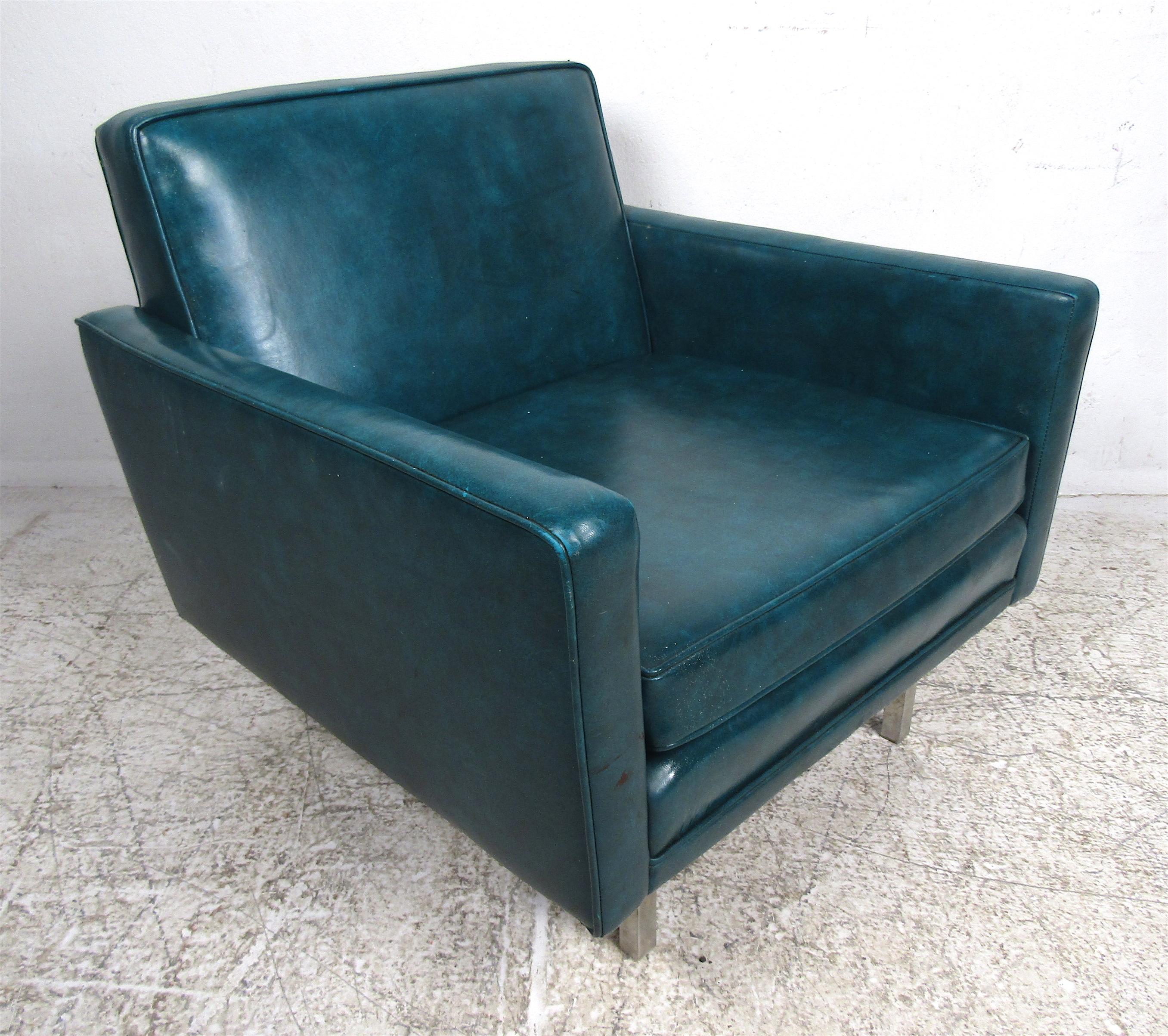 A lovely Mid-Century Modern club chair covered in green vinyl. The low armrests, thick padded cushion, and sturdy metal legs add to the allure. A comfortable and stylish piece that looks great in any seating arrangement. Please confirm the item