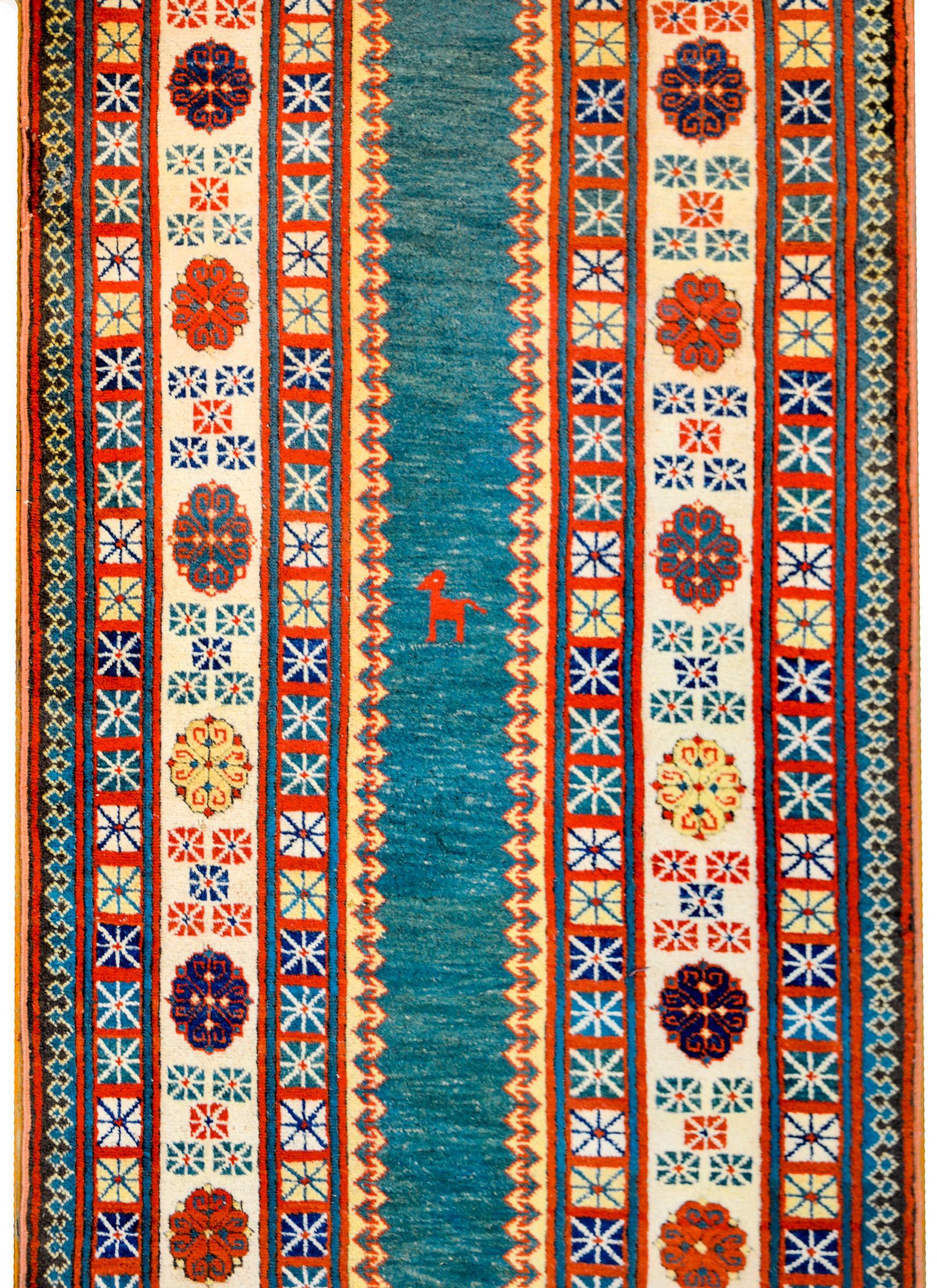 A beautiful 21st century Turkish Talish runner with a narrow indigo central field with a crimson goat in the center. The border is extremely wide with several geometric and stylized floral patterned stripes, all woven in indigo, crimson, yellow, and