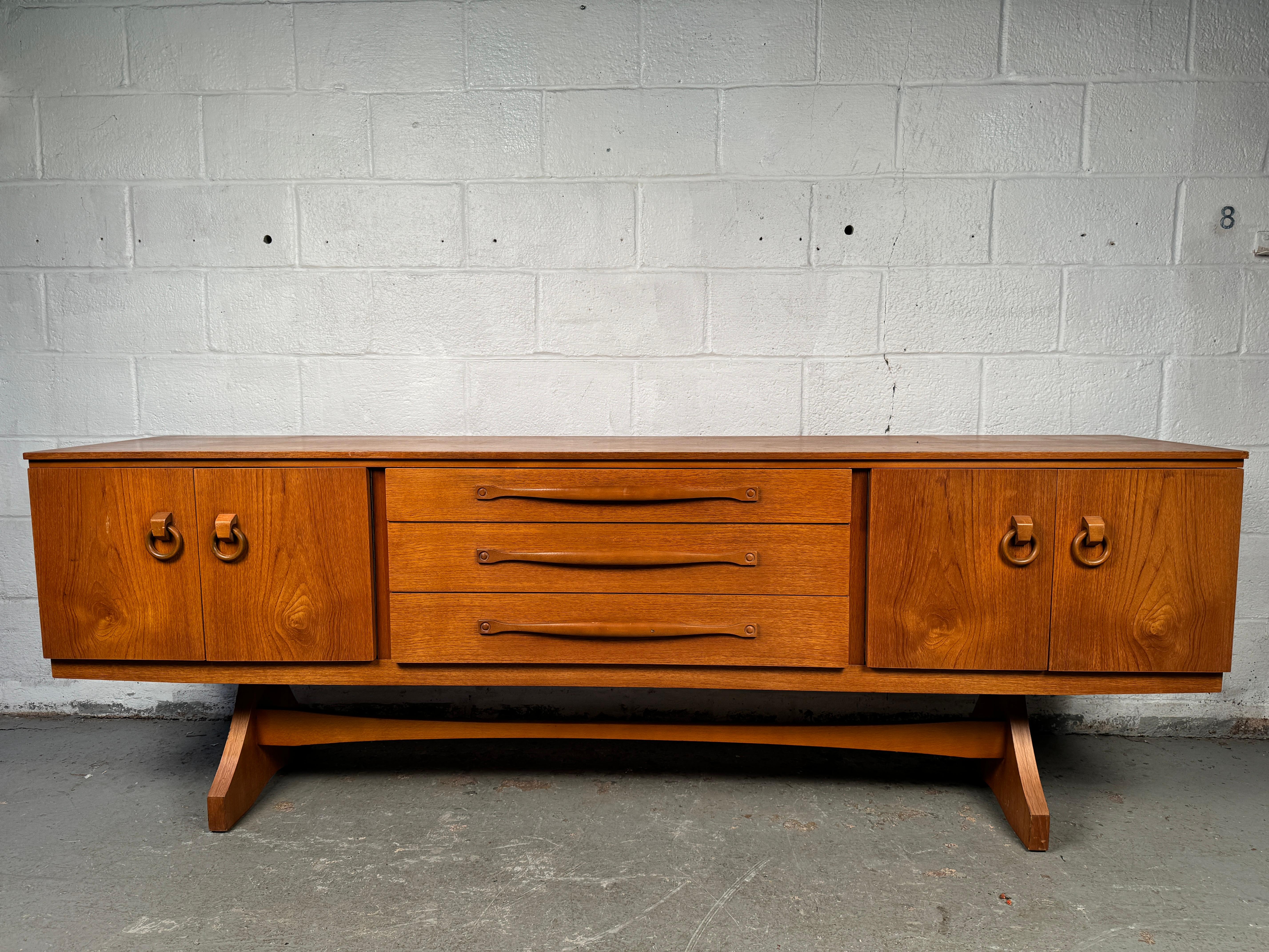 Aggiungi una raffinatezza senza tempo alla tua casa con questa splendida credenza vintage in teak, sapientemente realizzata dal rinomato produttore di mobili britannico Beautility durante l'epoca d'oro del design di metà secolo. Con le sue linee