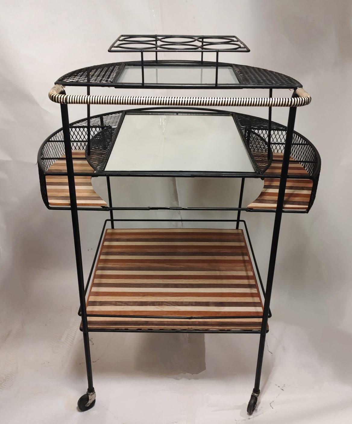 Beautiful black wrought iron Bar Cart from the 1950s, very minimal and simple design yet sophisticated and elegant. With recently attached wood-striped trays, and other trays in opaque glass and mirror. It comes with a  whimsical original set of