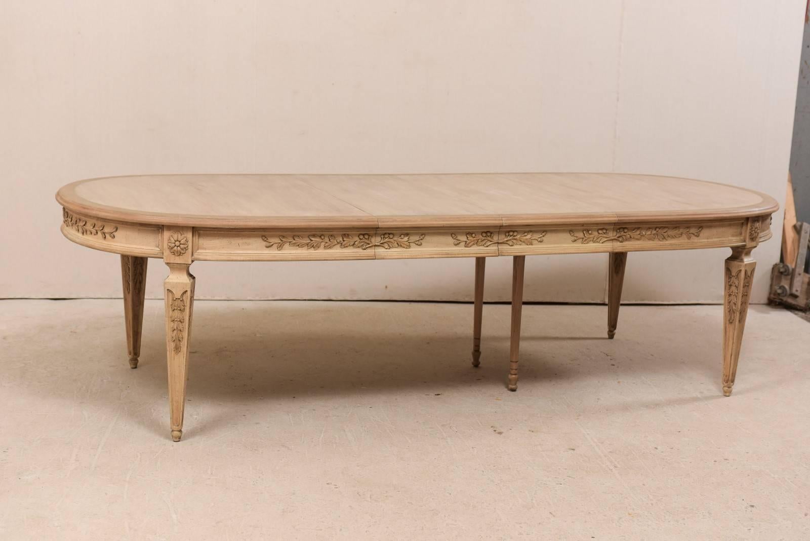 A vintage American dining table with beautifully carved apron and legs. This ash wood dining-room table features an oval-shaped top with ornately carved foliage motif about all sides of the rounded apron, and carved flowers at each knee. This