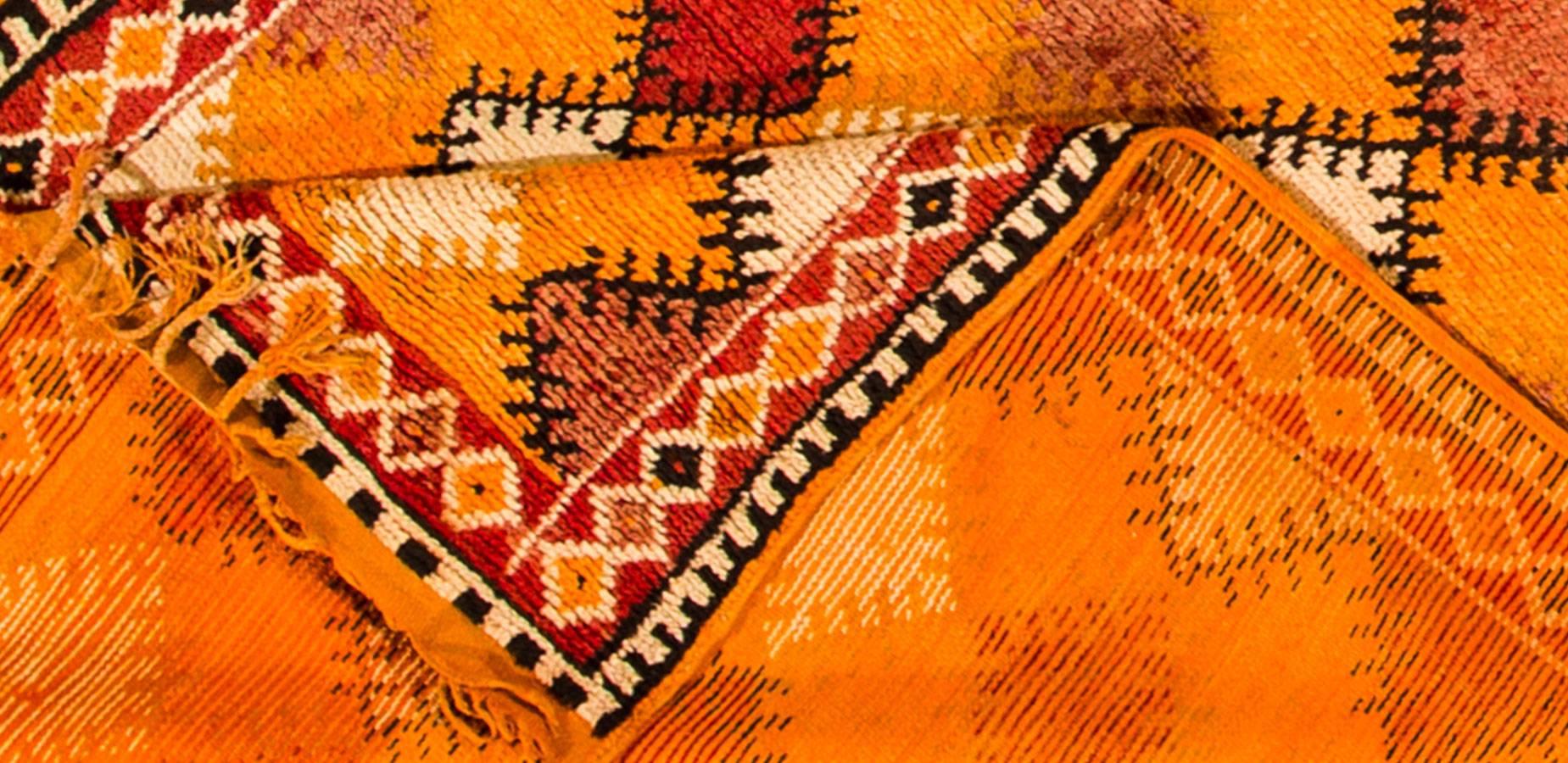 Beautiful Vintage hand-knotted Moroccan rug with a repeating geometric design on an orange field. Accents of yellow, red, and brown throughout the piece.

This rug measures 4'9