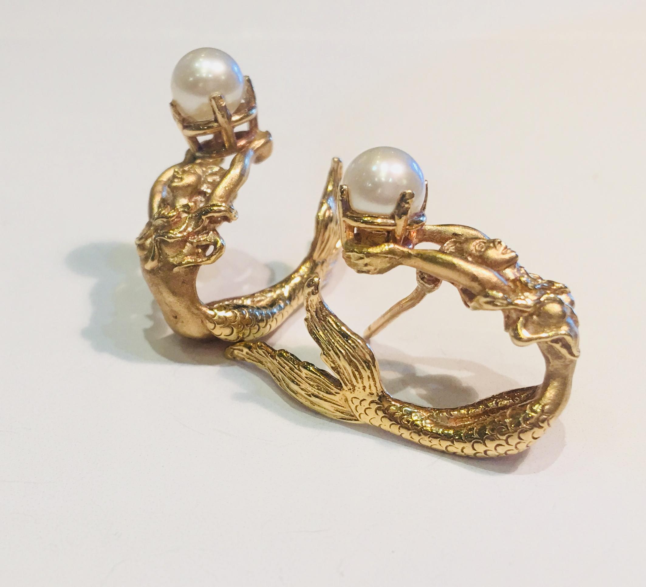 14 karat yellow gold earrings are a pair of beautifully detailed, 3 dimensional mermaids holding one prong set lustrous white pearl, with graceful tails that wrap around the ears.

Pearls measure 5.65 mm each.   Earrings measure 26.17 mm x 21 mm x