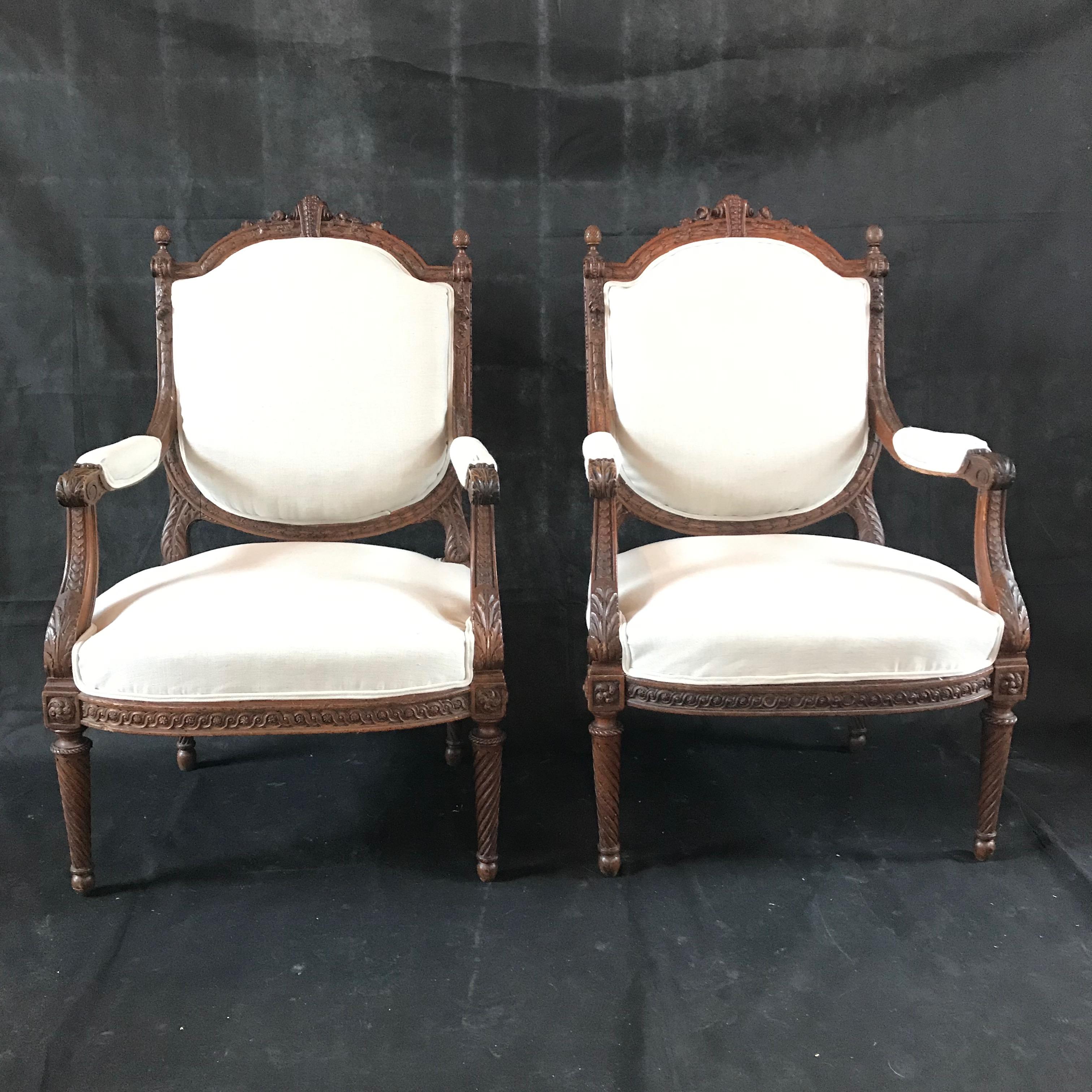 A stunning sturdy pair of elegant French Louis XVI fauteuils armchairs having intricately carved details of flowers, leaves, scrolls, and traditional motif decorative bands. The chairs have been newly professionally upholstered in a French vintage