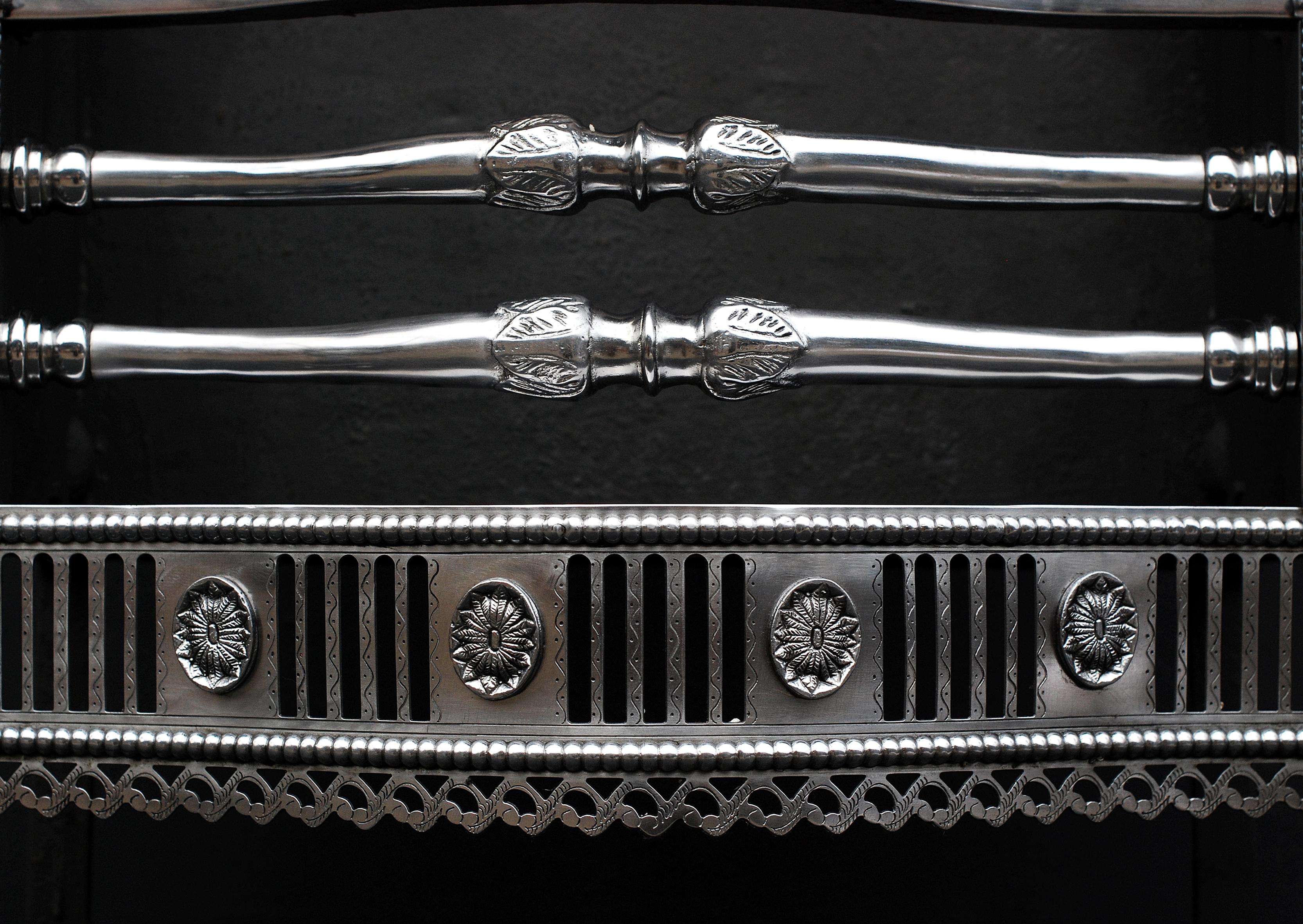 A beautifully engraved polished steel English Georgian style firegrate. The pierced, engraved fret with flutes and oval pateras with beading above and below, the side wings with bell drops, beading and circular pateras, the tapering cylindrical legs
