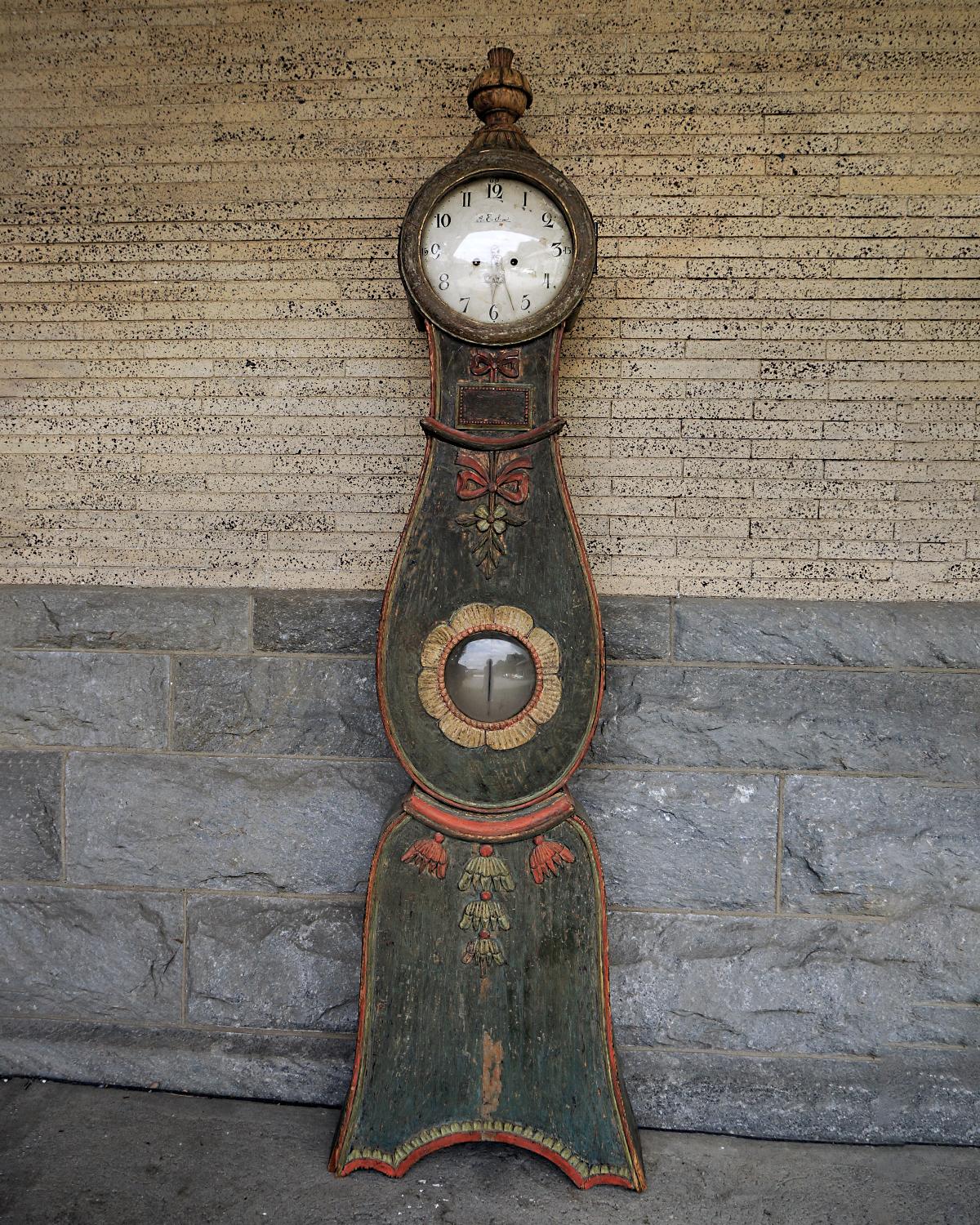Swedish tall case clock in original decorative paint. The original works with signed dial are from the village of Mora and were probably carried back to Ljusdal where the case was made. The bonnet is topped with a carved urn finial, and the body