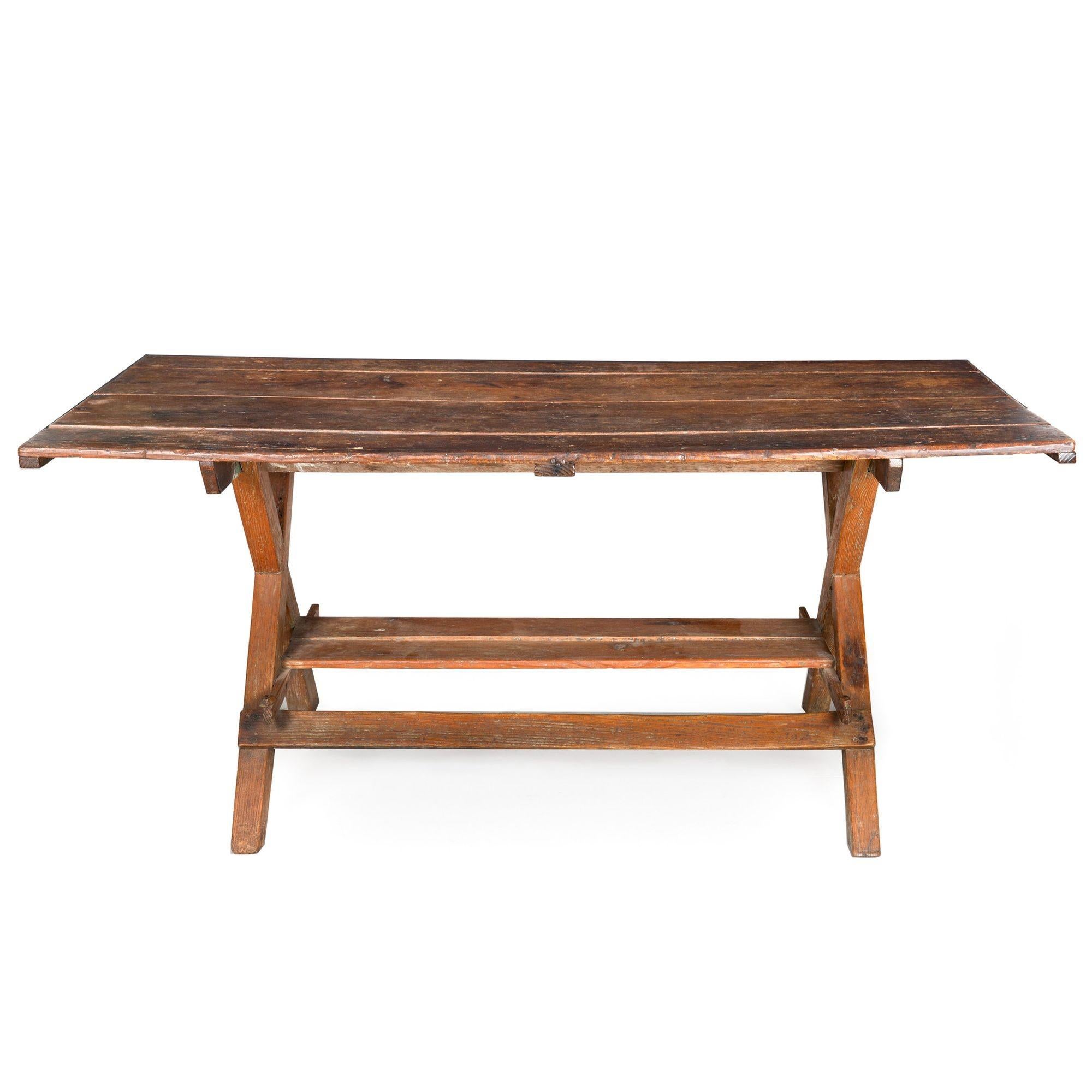 This remarkable American trestle table is distinguished by its impressive surface patina. It showcases an X-form leg profile crafted from solid oak, complemented by a shelved stretcher at the bottom. The top of the table consists of four solid