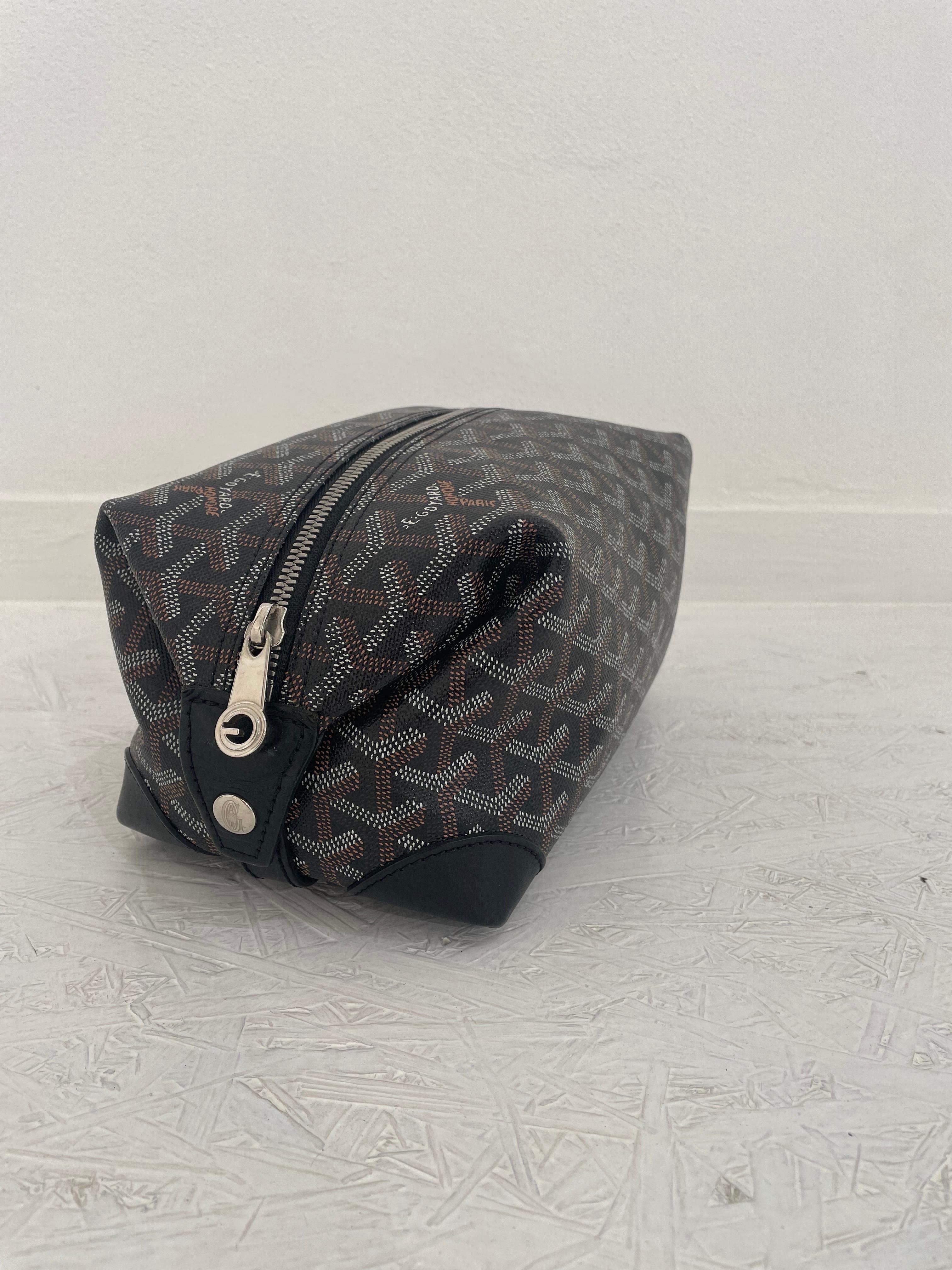 Beauty Goyard with classic pattern and black leather details. Zip closure and two side clip buttons to adjust the capacity. Ochre interior. In perfect condition only a few small marks on the corners with original dust. 
24 cm wide
13 cm high 
Depth