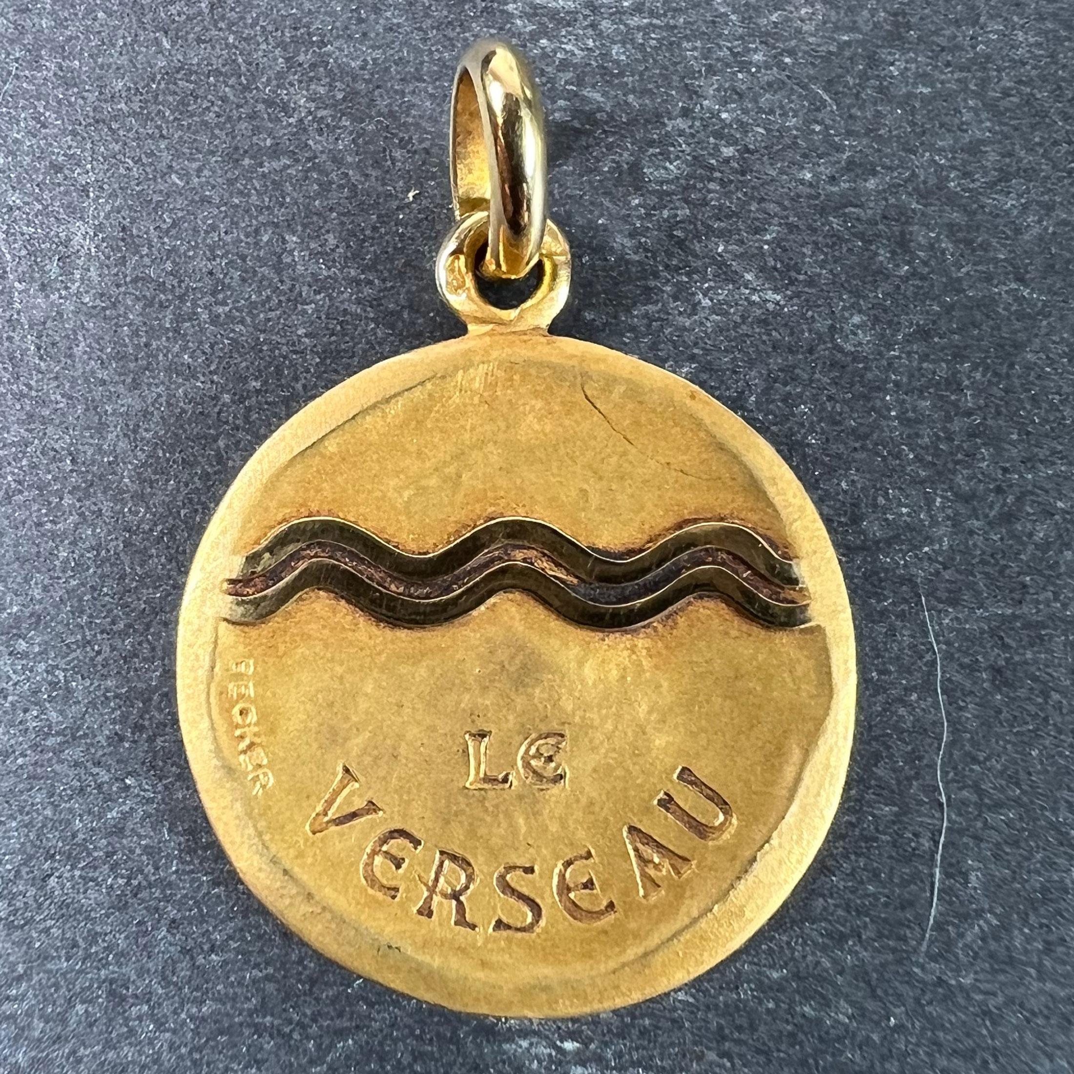 A French 18 karat (18K) yellow gold charm pendant depicting the Zodiac star-sign of Aquarius as the astrological symbol for the sign in polished gold on a matt gold convex recessed base, with the phrase 'Le Verseau' beneath. Signed Becker and