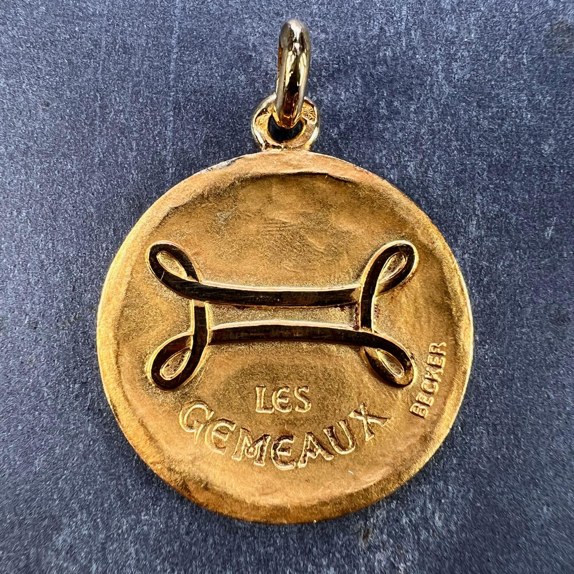 A French 18 karat (18K) yellow gold charm pendant depicting the Zodiac starsign of Gemini as the astrological symbol for the sign in polished gold on a matt gold convex recessed base, with the phrase 'Les Gemeaux' beneath. Signed Becker and stamped