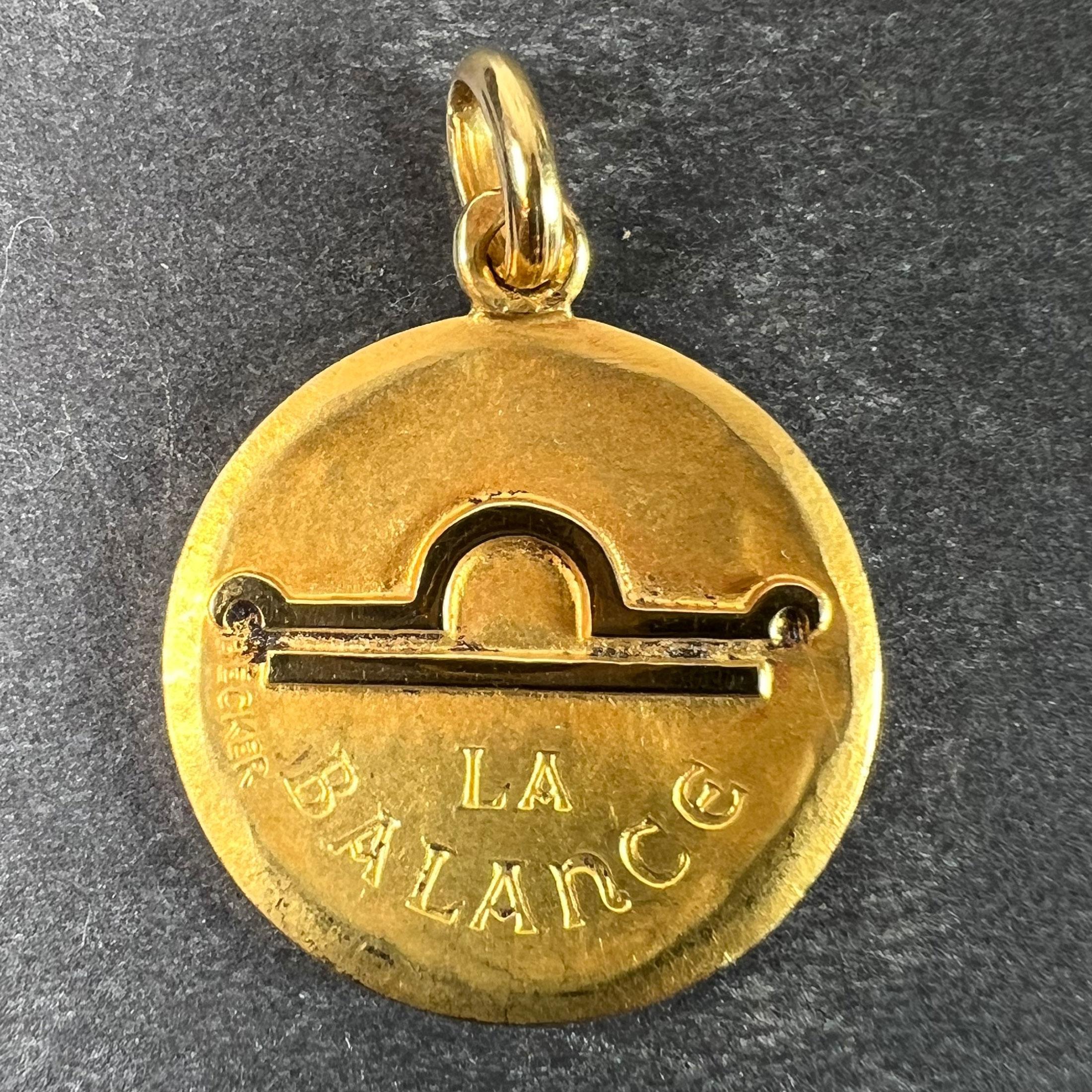 A French 18 karat (18K) yellow gold charm pendant depicting the Zodiac star-sign of Libra as the astrological symbol for the sign in polished gold on a matt gold convex recessed base, with the phrase 'La Balance' beneath. The reverse depicts a hand