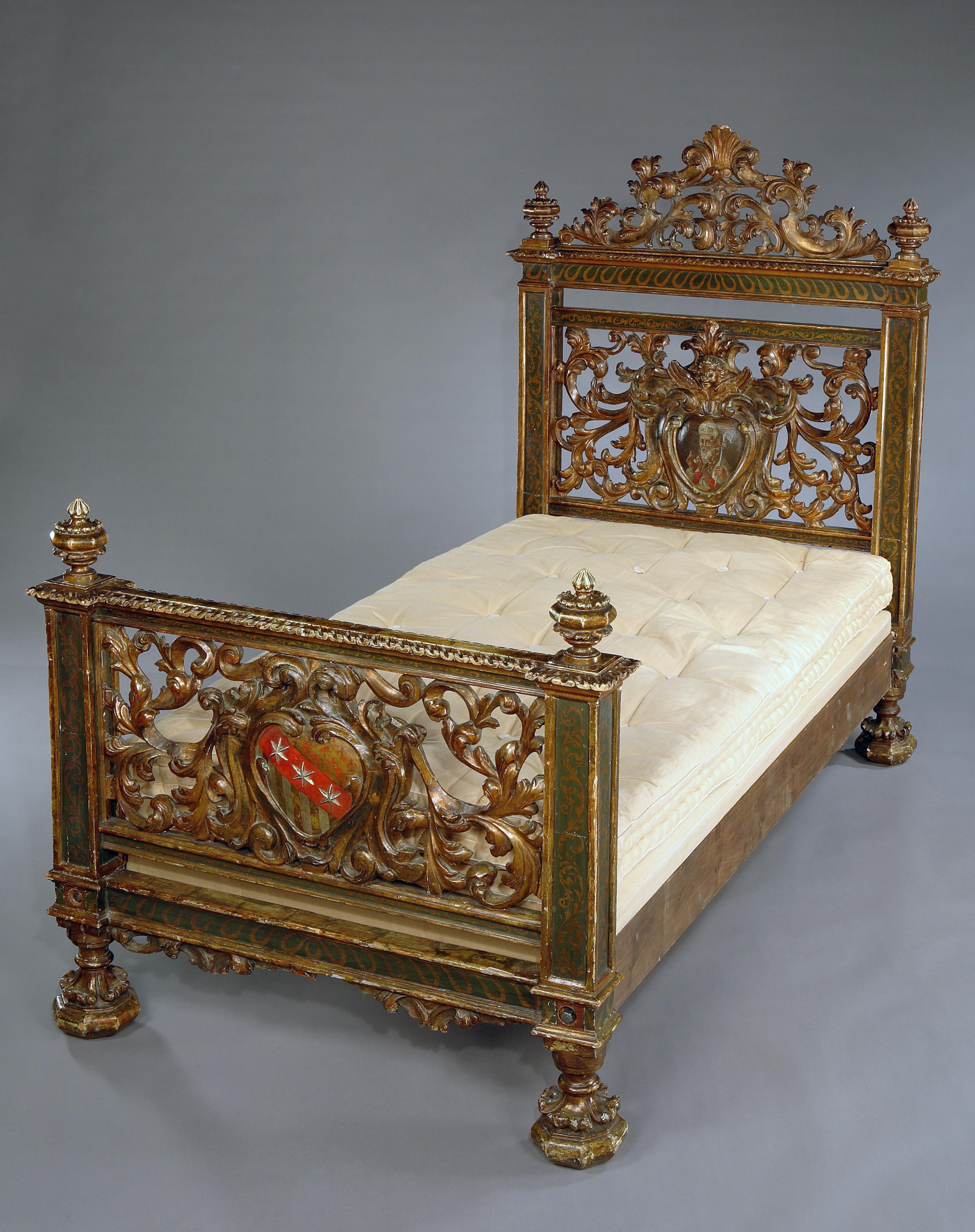 The headboard is surmounted with a carved cresting and turned finials at each end, and the frame painted with scrollwork. The centre of the headboard has a cartouche containing a painting of a coat of arms, surrounded by profuse, stylized, acanthus