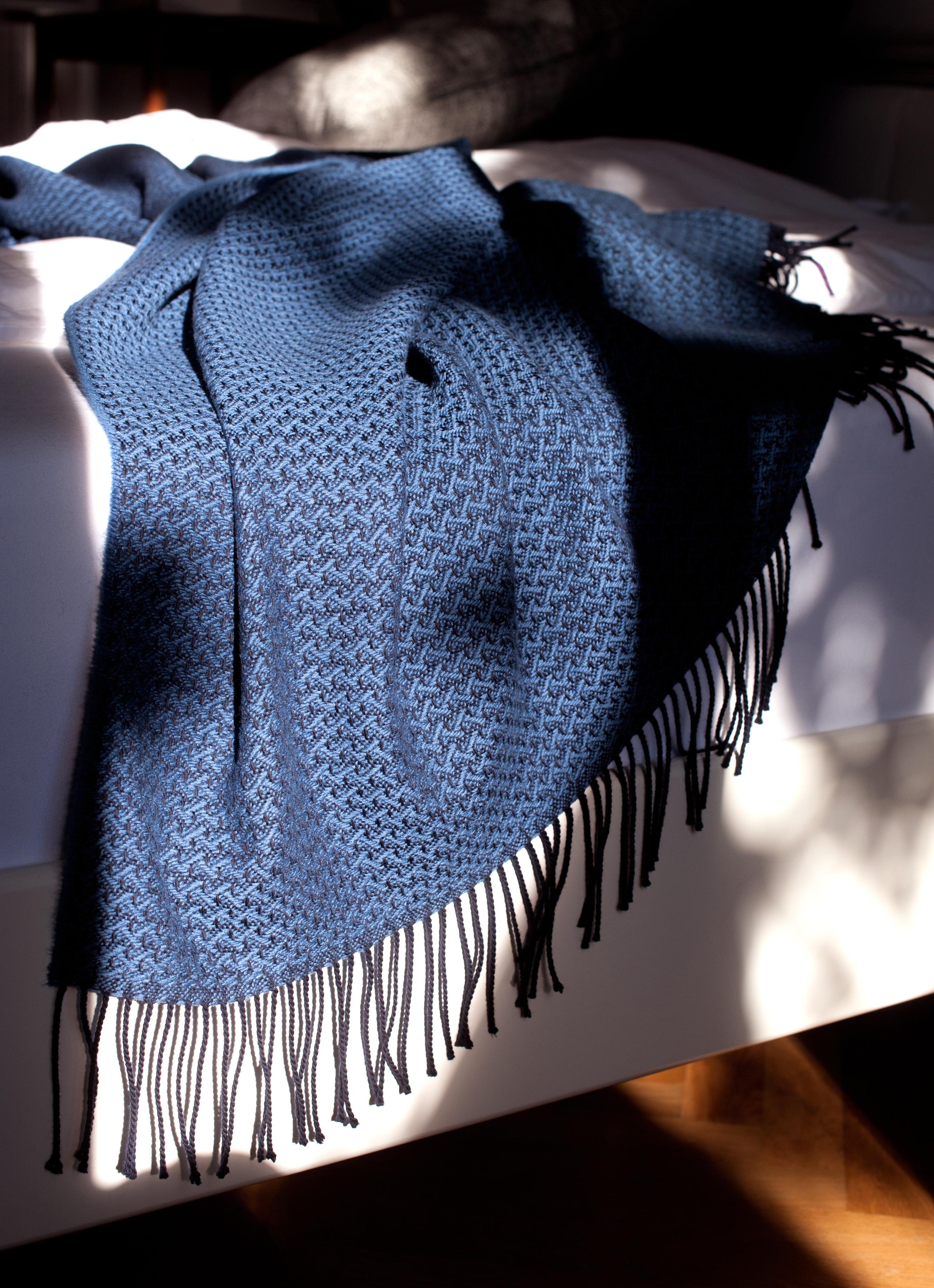 Entworfen in Berlin von Catharina Mende, gewebt aus 100% extrafeiner Merino in Schottland: Dieser exquisite Bettüberwurf in der Farbe Blau, gewebt in Schottland aus feinster extrafeiner Merino, ist ein Stück Schönheit und Eleganz für jedes