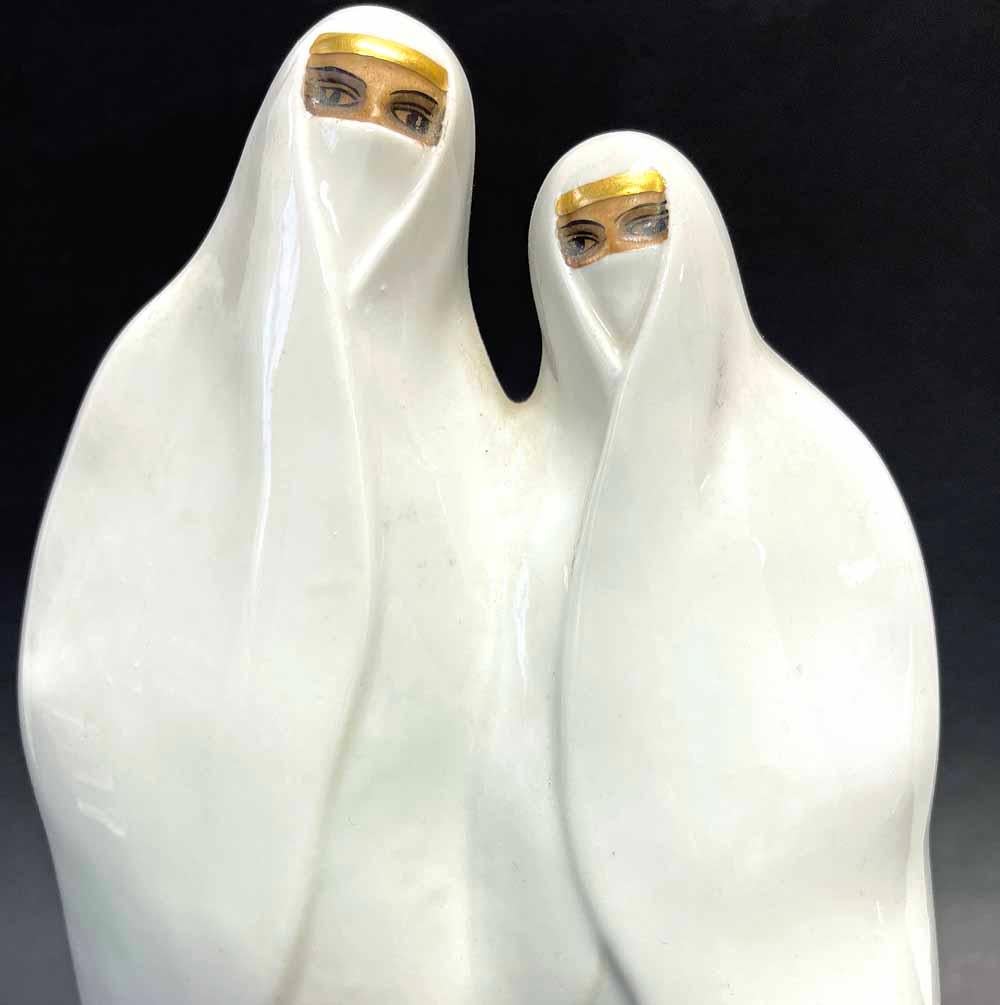 Rare et saisissante, cette sculpture et veilleuse en porcelaine représente deux femmes bédouines vêtues de robes d'un blanc éclatant, encadrées par des bandeaux en or et un sol en or sous leurs pieds.  La forme lisse et liquide de leurs formes