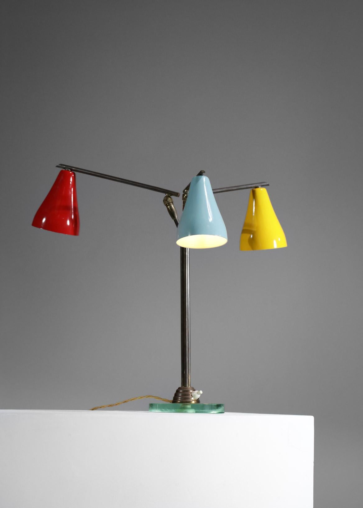 Italian desk or bedside lamp from the 1960s attributed to Fontana Arte. Asymmetrical structure with three solid brass arms, glass base and red, yellow and blue lacquered metal shade (length of the arms red 25 cm, yellow 20 cm, blue 15 cm). Excellent