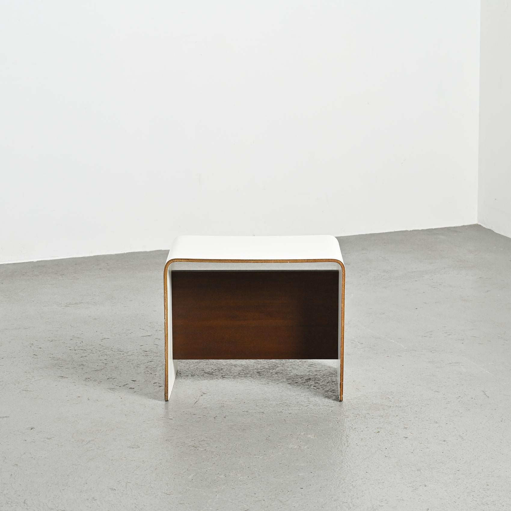 
Table de nuit conçue par Pierre Guariche pour les appartements de La Plagne et de Bandol.

Cette pièce minimale et fonctionnelle est fabriquée en contreplaqué cintré en forme de U, finie avec un plateau en stratifié blanc et un châssis plaqué bois.