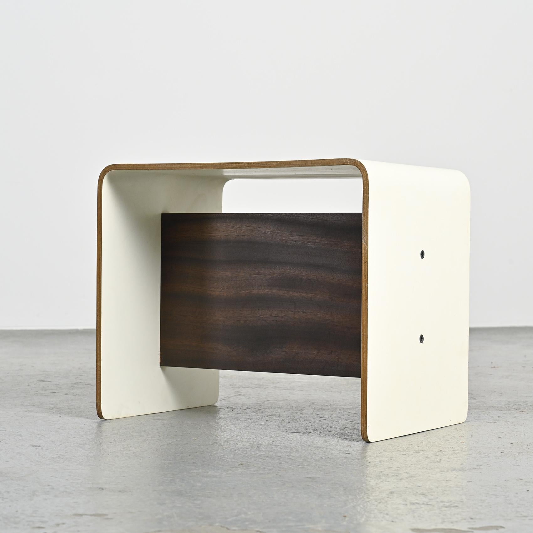 
Table de nuit conçue par Pierre Guariche pour les appartements de La Plagne et de Bandol.

Cette pièce minimale et fonctionnelle est fabriquée en contreplaqué cintré en forme de U, finie avec un plateau en stratifié blanc et un châssis plaqué bois.