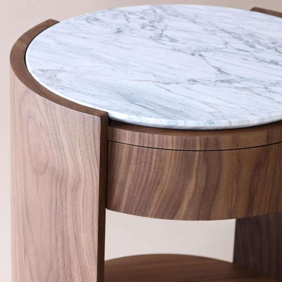 El complemento perfecto para un espacio de descanso tranquilo y luminoso.
La Mesilla de Noche Dama une la calidez del nogal con la pureza del mármol blanco, revelando un delicado equilibrio entre contraste de materiales y armonía. Con sus tonos