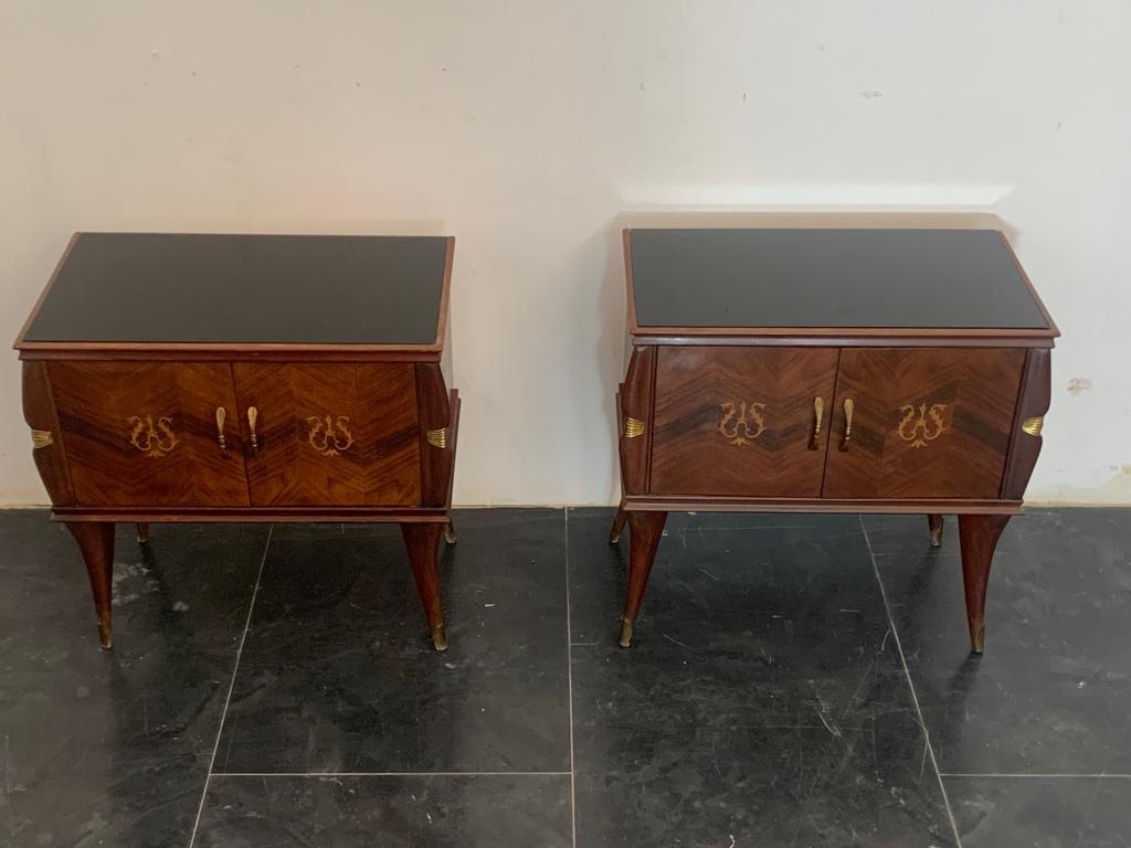 Pair of 1950s rosewood bedside tables with brass handles, finials and details. Black glass top. Slight wear due to age and use.
Packaging with bubble wrap and cardboard boxes is included. If the wooden packaging is needed (fumigated crates or boxes)