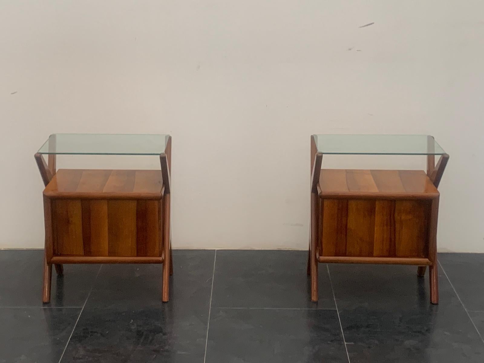 Pair of rosewood and glass bedside tables, 1960s. Excellent quality of materials and construction, generous thicknesses, beautiful rosewood selection. The sides have diagonal pilasters that intertwine, supporting the body and glass top. In the