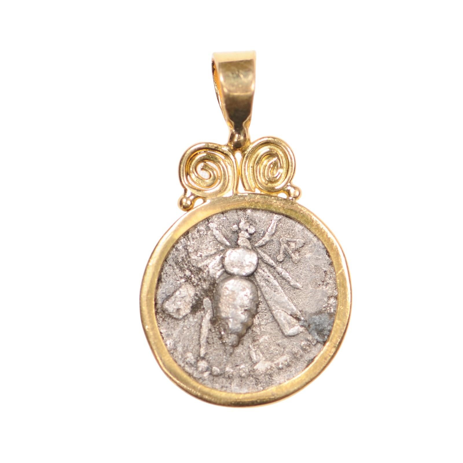 An AR drachm [coin] minted in ancient Phoenicia, circa 2nd century BC., set in 22k gold. On the obverse side, a bee with monogram to its right. On the reverse side, a stag standing (right facing), with a palm tree behind and APAΔIΩ[N] downward to