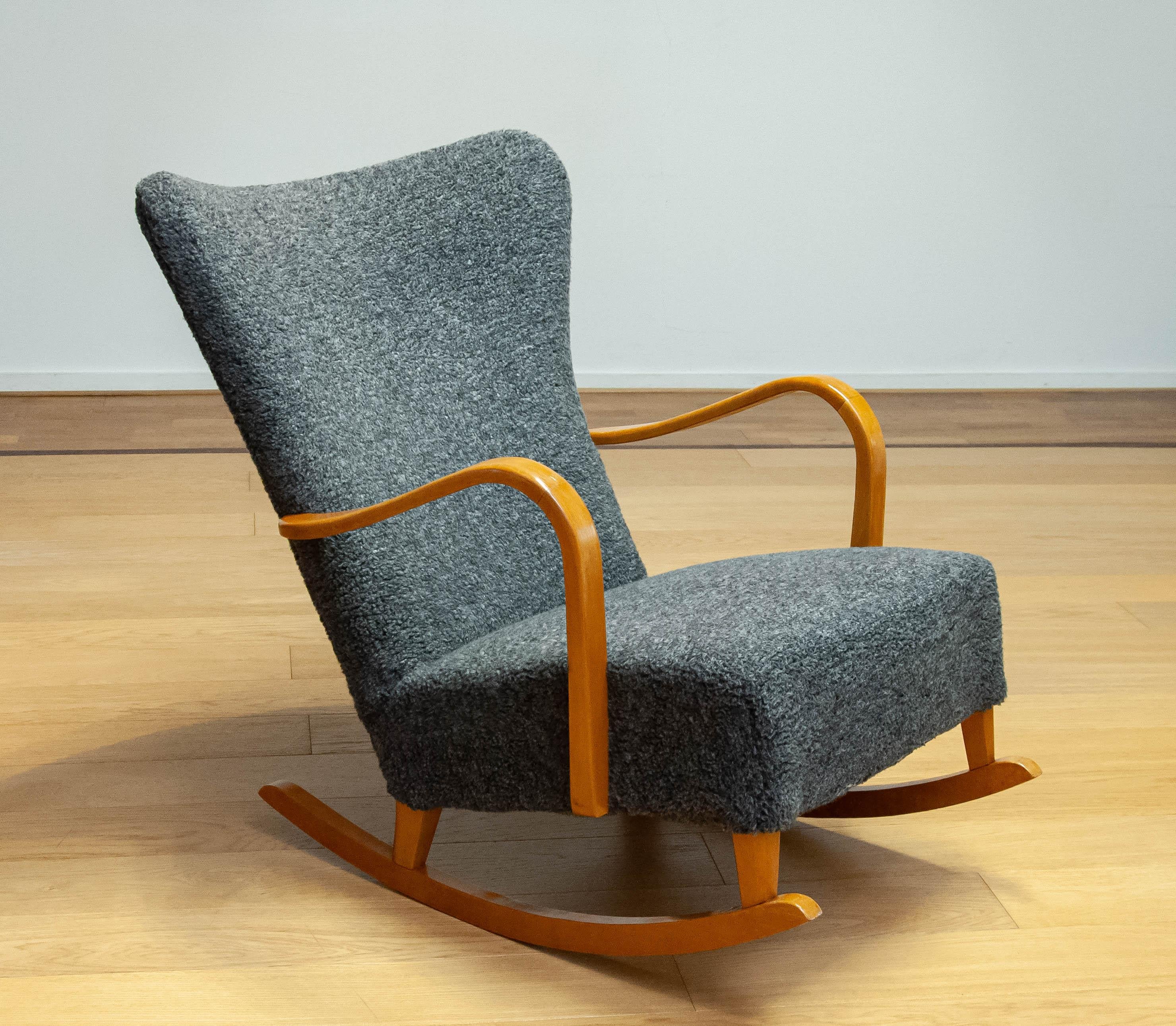 Magnifique fauteuil à bascule des années 1940 tapissé d'un tissu bouclé gris mélangé. Ce tissu date d'une période plus tardive et est en bon état. Le hêtre sélectionné pour la construction du cadre ressemble à du bois de tigre doré. Associée au
