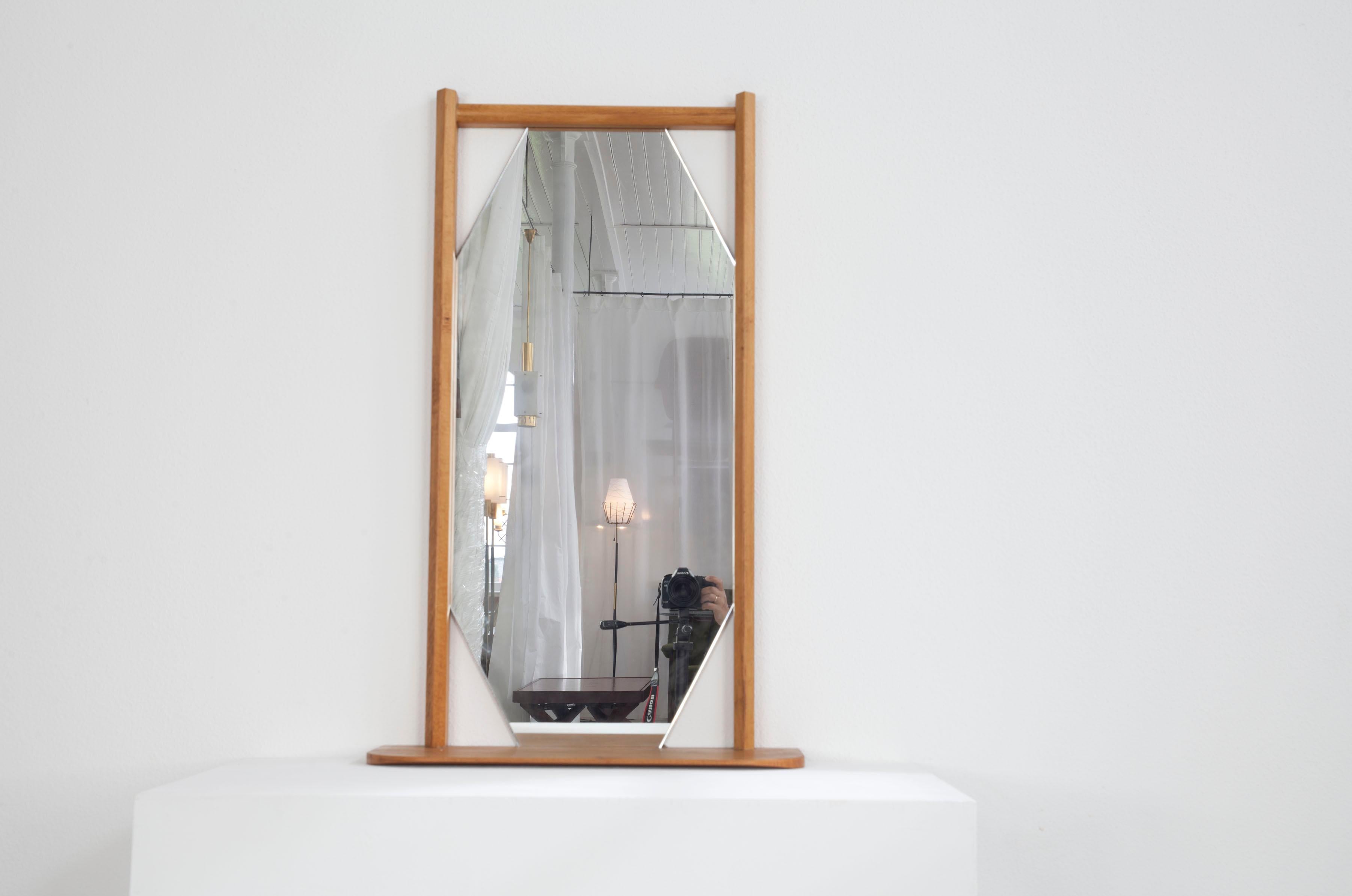This Italian wall mirror dates from the 1960s. The mirror itself has the shape of an elongated hexagon. The beechwood frame, on the other hand, is rectangular. At the bottom of the frame there is a small practical shelf on which small items can be