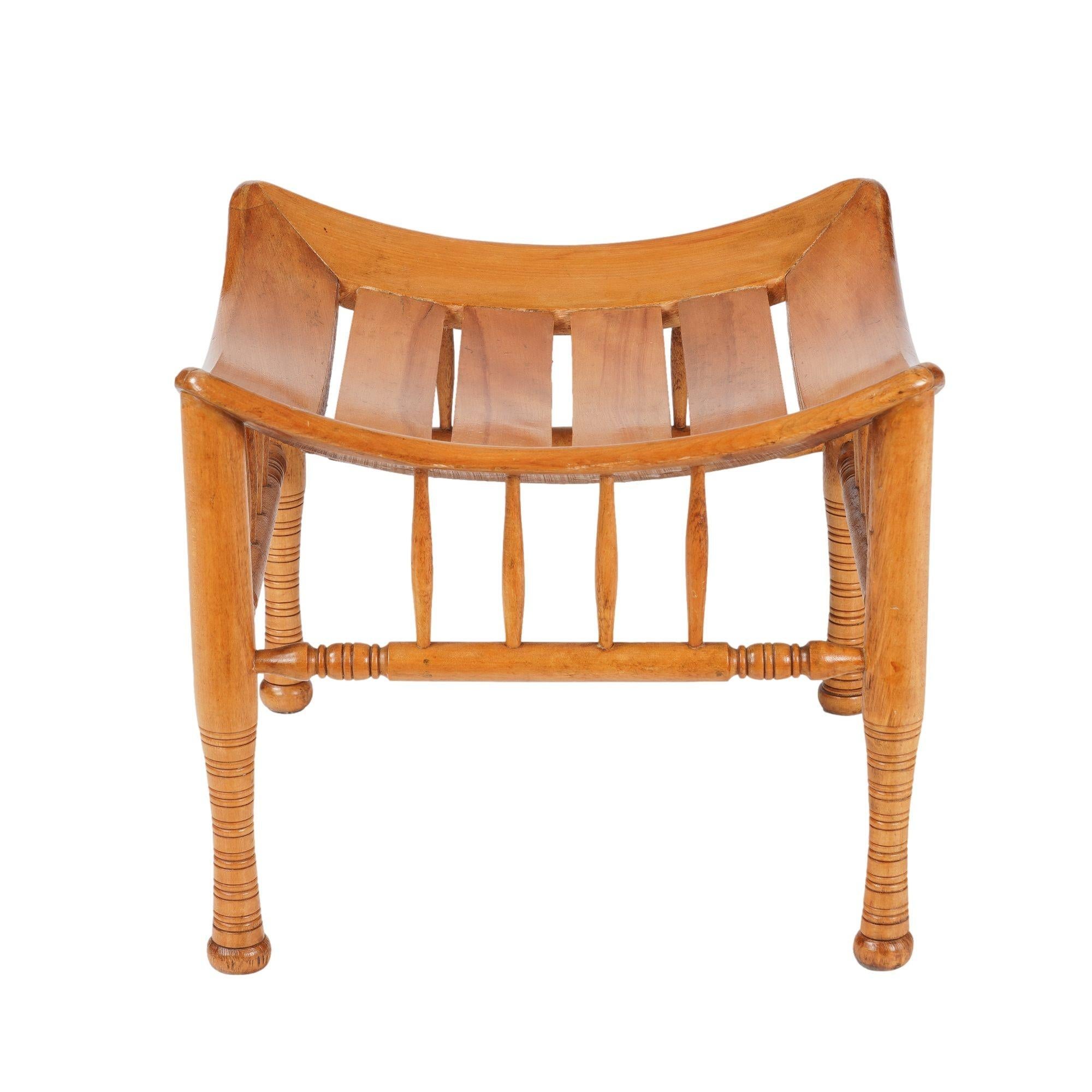 Sgabello in stile egiziano di Tebe in legno di faggio con finitura naturale, secondo un modello archeologico. Le quattro gambe tornite sono unite da una barella mediale scatolata, ciascuna con quattro montanti verticali torniti, alla struttura a