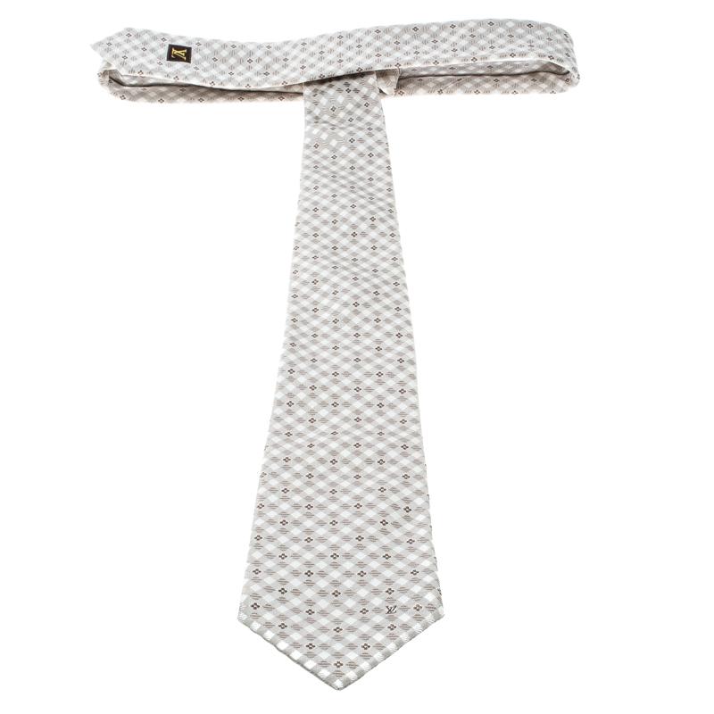 This beige and cream tie from Louis Vuitton is what every man needs to have. Made of 100% silk, it features the signature monogram design as well as a checked pattern all over it and at the back it has a brand label keeper loop. The 9 cm tie is sure