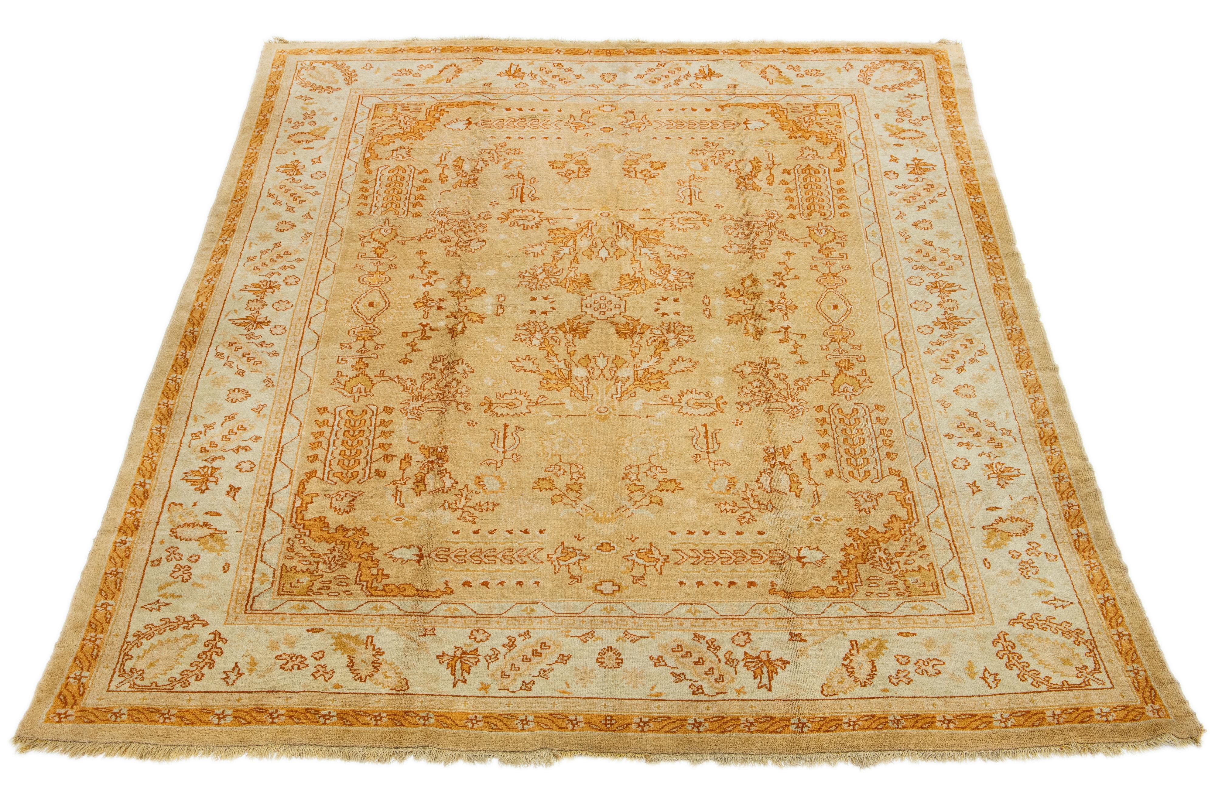 Unique Turkish Oushak rug. Hand-knotted with premium wool. Tan beige field, light blue border, vibrant floral design with orange and golden accents.

This rug measures 9'5'' x 12'8''.
