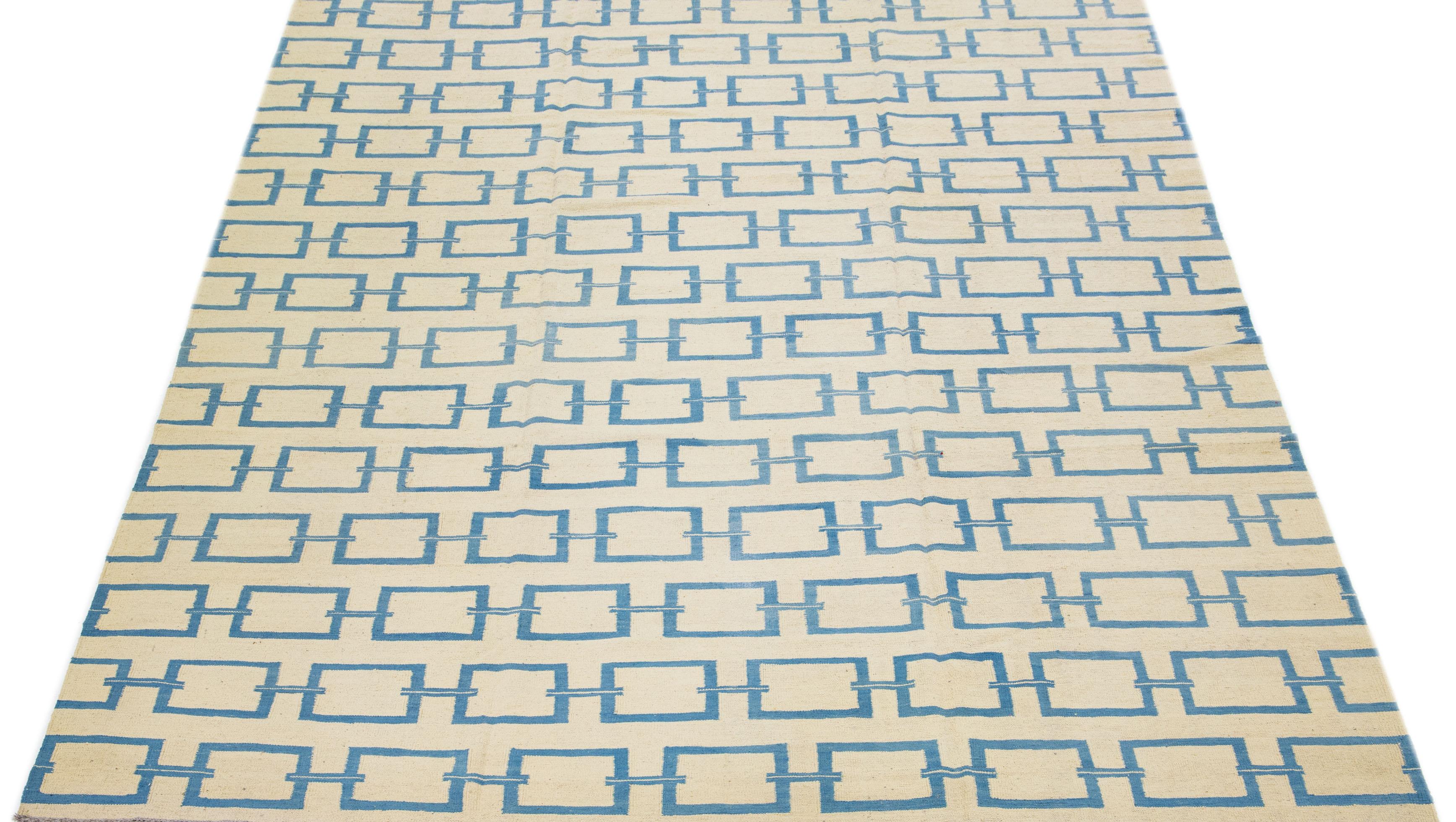 Dieser zeitgenössische Kilim-Teppich ist sorgfältig von Hand gewebt und hat ein dominantes beigefarbenes Feld, das durch komplizierte geometrische Muster in Blautönen hervorgehoben wird, die subtile, aber elegante Akzente setzen.

Dieser Teppich