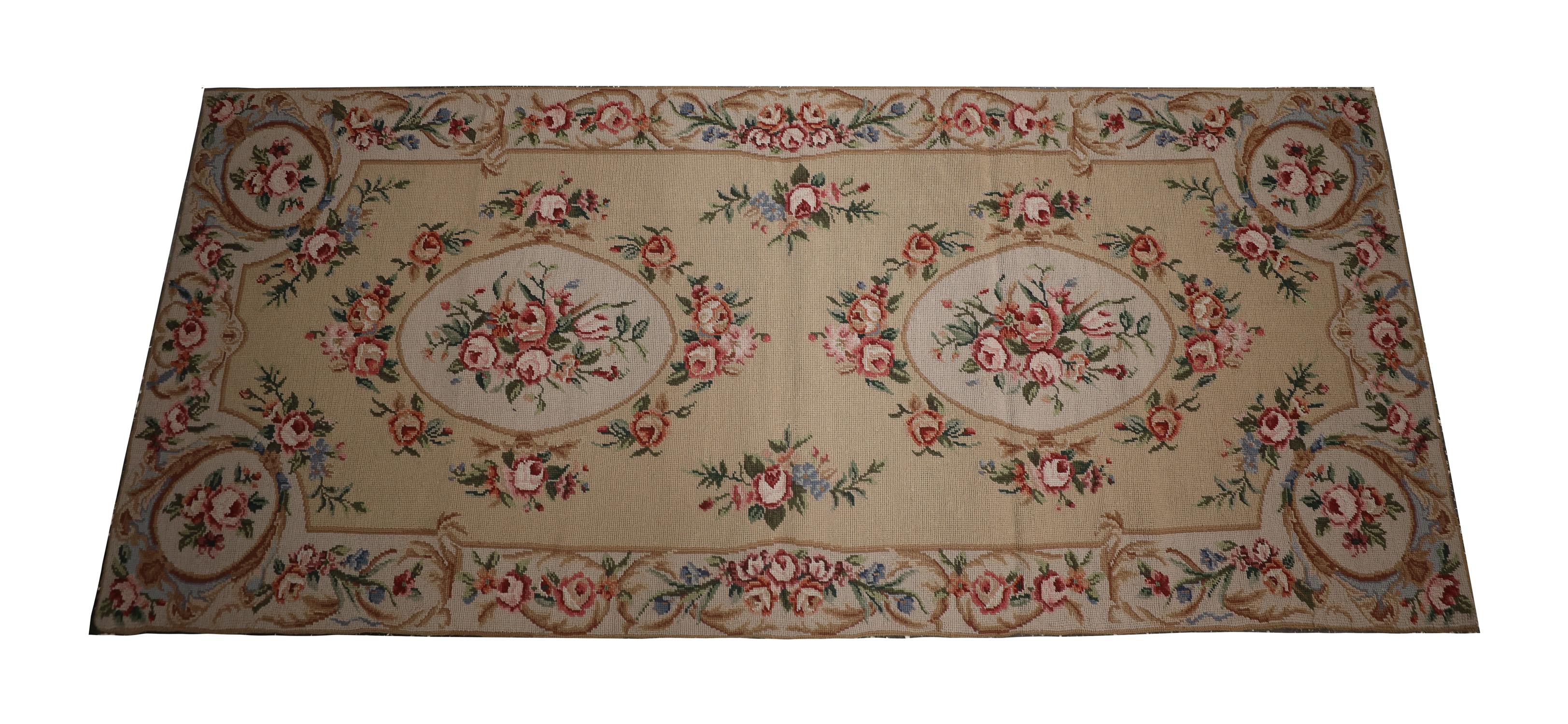 This elegant needlepoint rug was woven by hand in the early 21st century, using traditional techniques and materials. The beautiful Aubusson design features two oval, floral medallions woven in accents of pink, ivory and green on a cream repeat