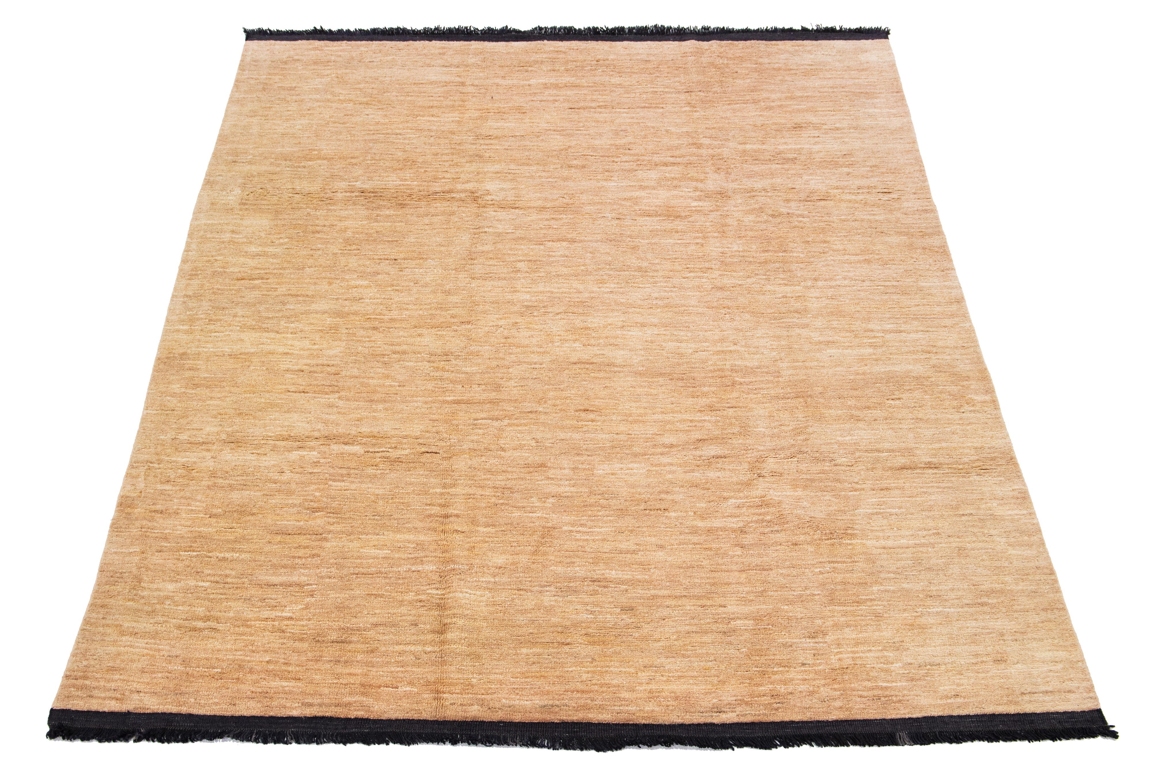 Ce tapis en laine fabriqué à la main, conçu dans le style Gabbeh, présente un motif uni souligné par des franges noires et un fond beige.

Ce tapis mesure 7'9