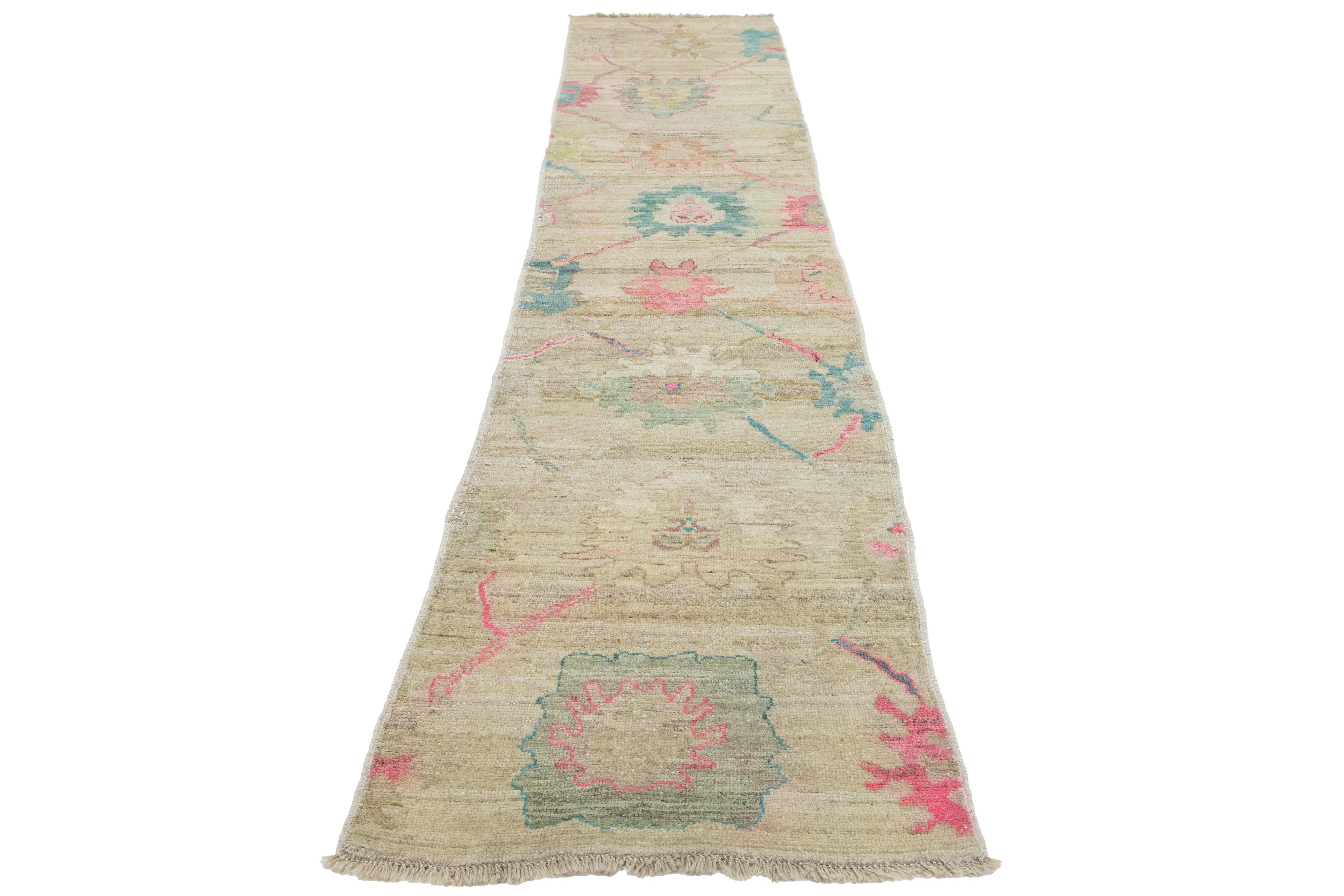Ein schöner, moderner, handgeknüpfter Oushak-Wollteppich mit beigem Feld. Dieses türkische Stück hat braune, blaue, grüne und rosafarbene Akzente in einem prächtigen Blumenmuster.

Dieser Teppich misst 2'10 x 14'8